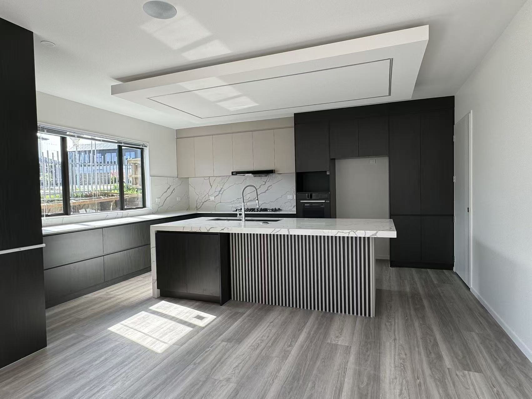 Modern kitchen with white marble countertops, black cabinetry, and a large window letting in natural light.