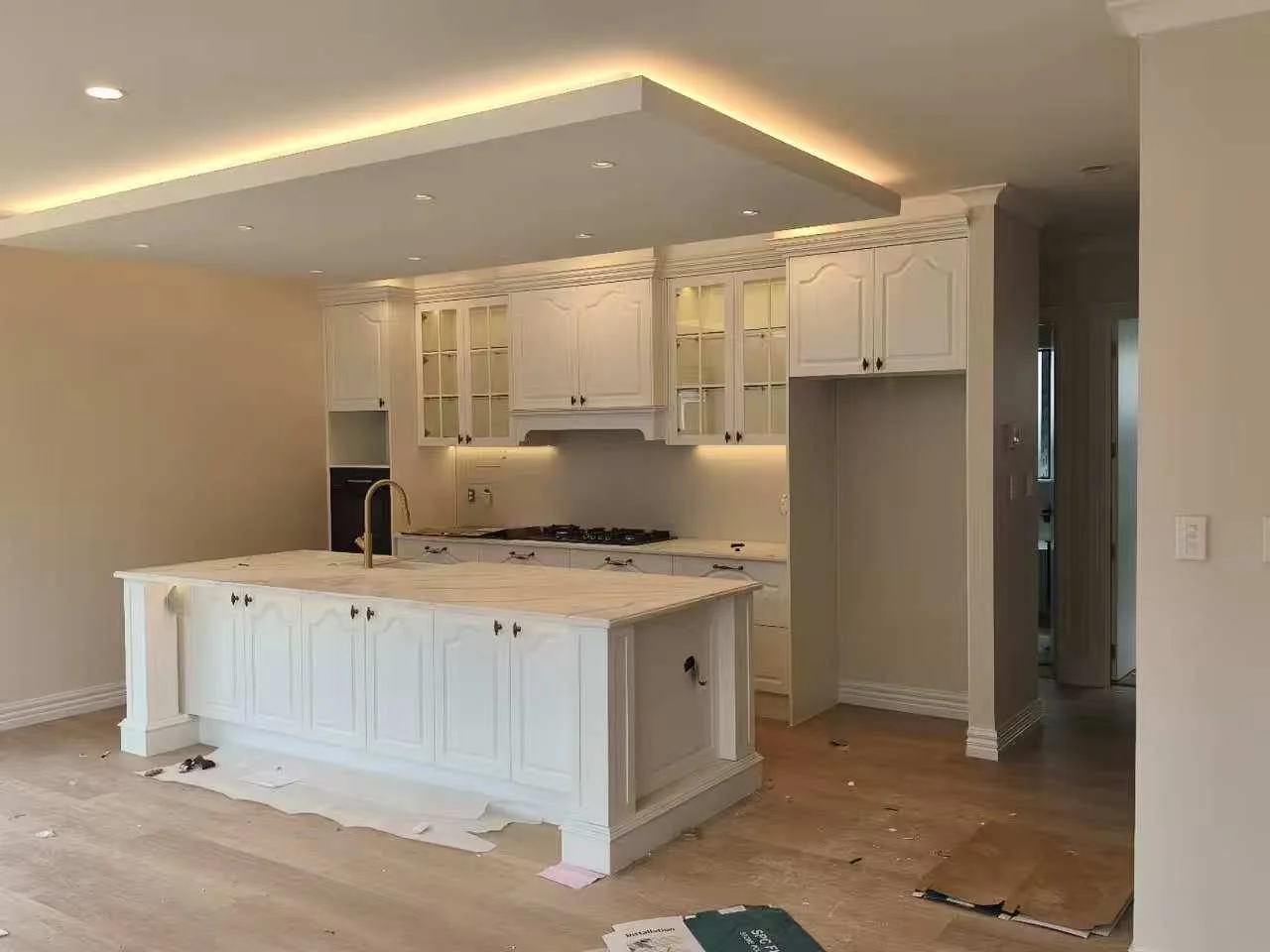 Kitchen with white cabinets and an island, ceiling lights, and hardwood flooring, in the process of being constructed or renovated.