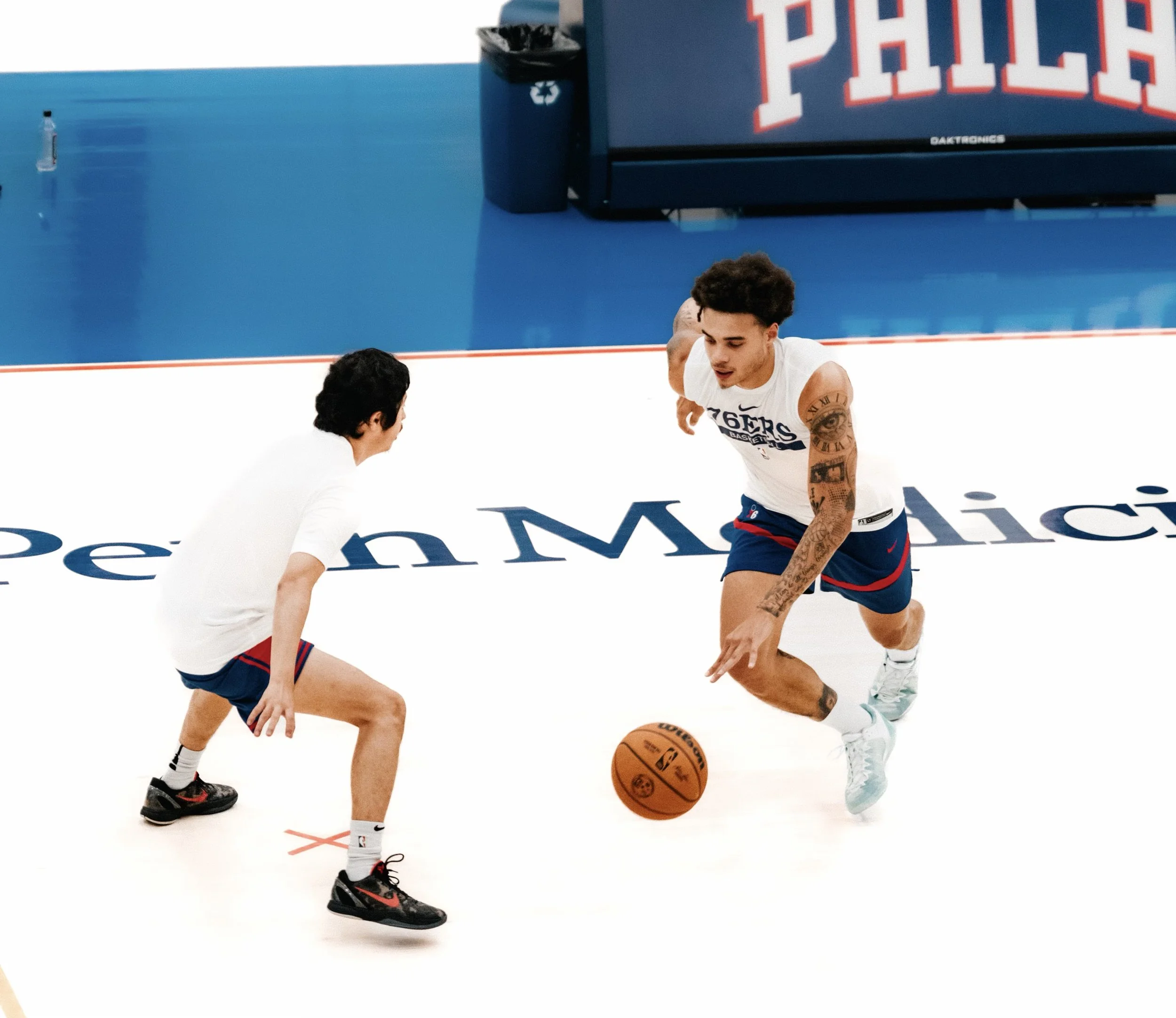 Two basketball players practicing on the court during a game. One player in a white T-shirt and shorts, and the other also in white, positioned to shoot or pass the ball.
