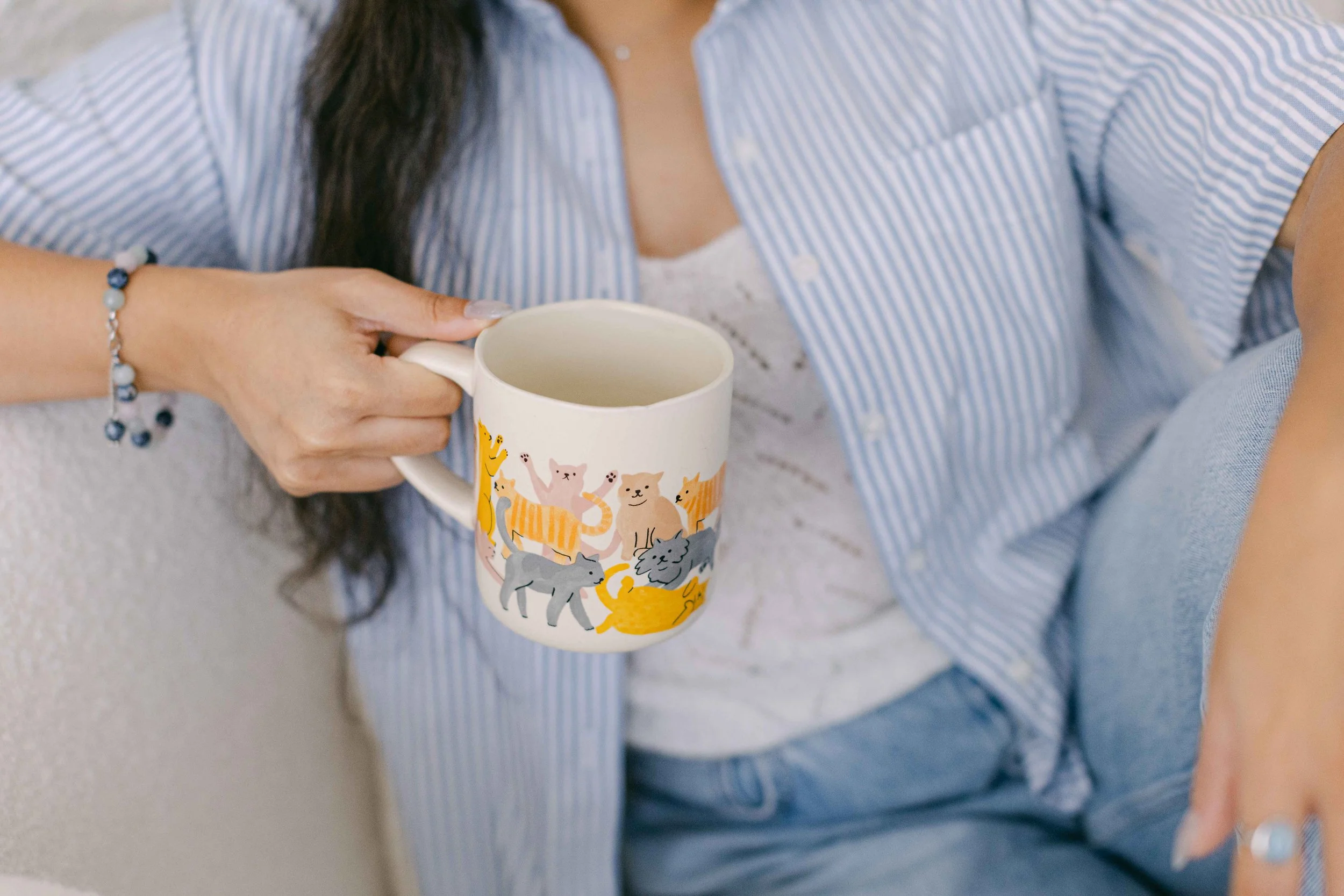 Close-up of a woman wearing a blue and white striped shirt, holding a colorful mug with animal illustrations, sitting on a light-colored sofa.