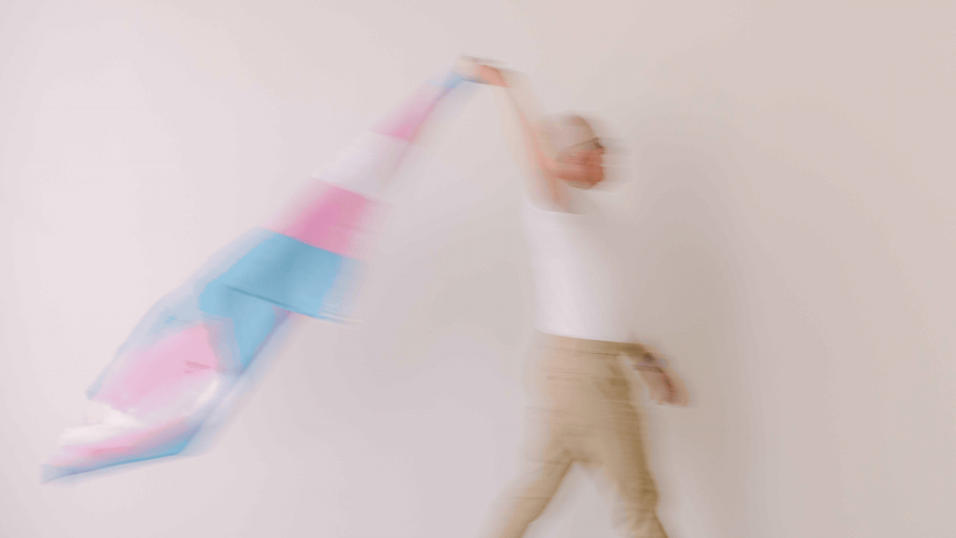 A person standing in front of a plain white wall at an art gallery or modern space, holding colorful, flowing fabric in motion, creating a sense of dynamic movement.
