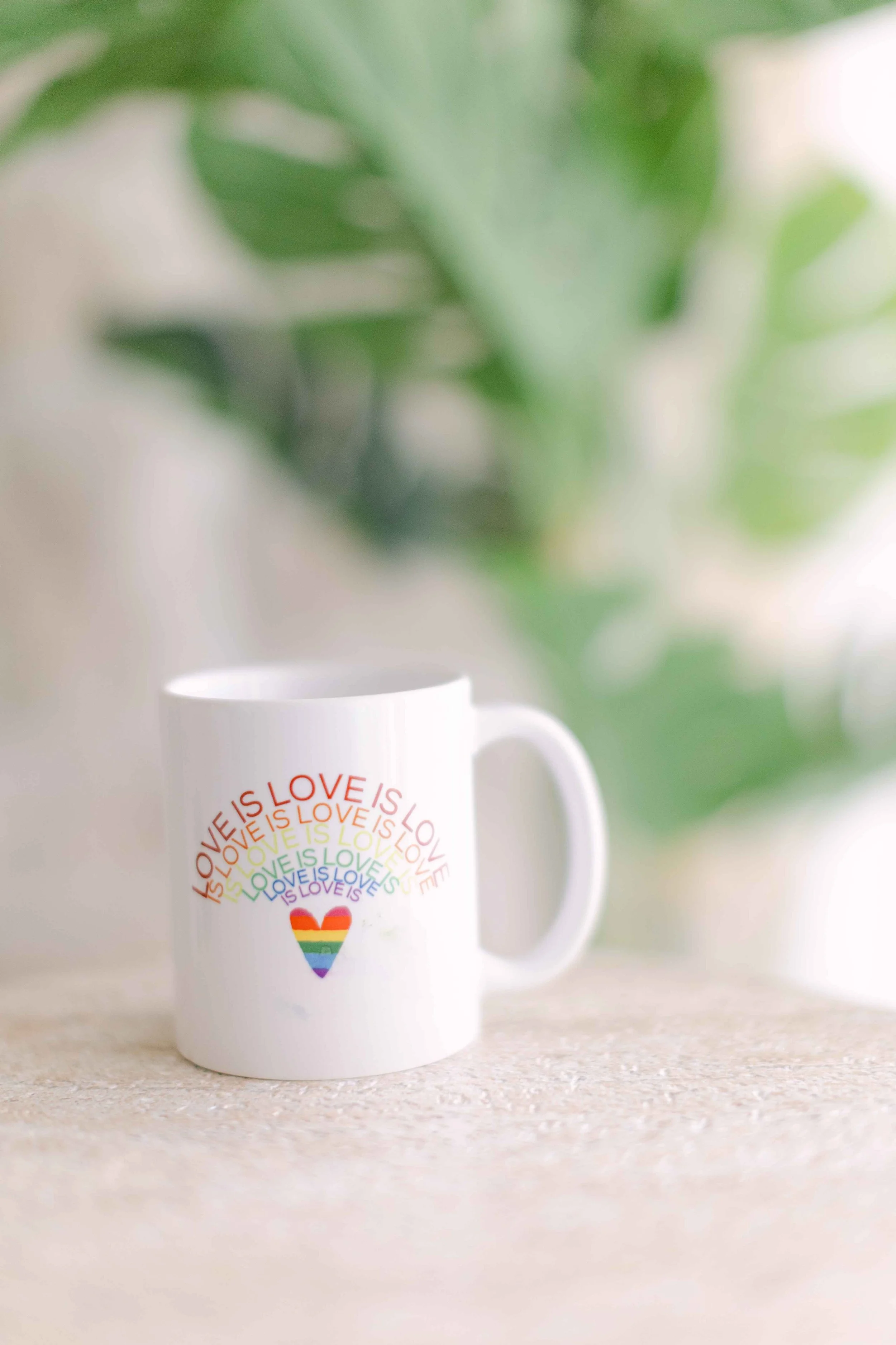White mug with a rainbow-colored heart and the words "LOVE IS LOVE" repeated in a circular pattern.