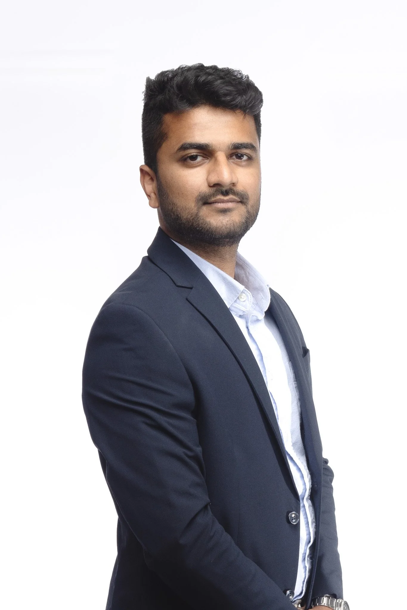 A young man in a gray suit white shirt stands against a white background, looking confidently at the camera.