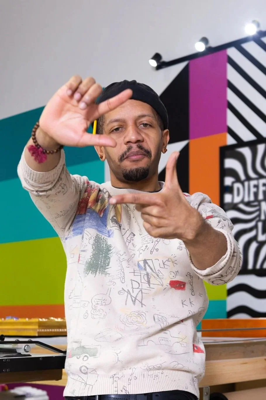 A man posing with his hands framing his face in front of a colorful background.