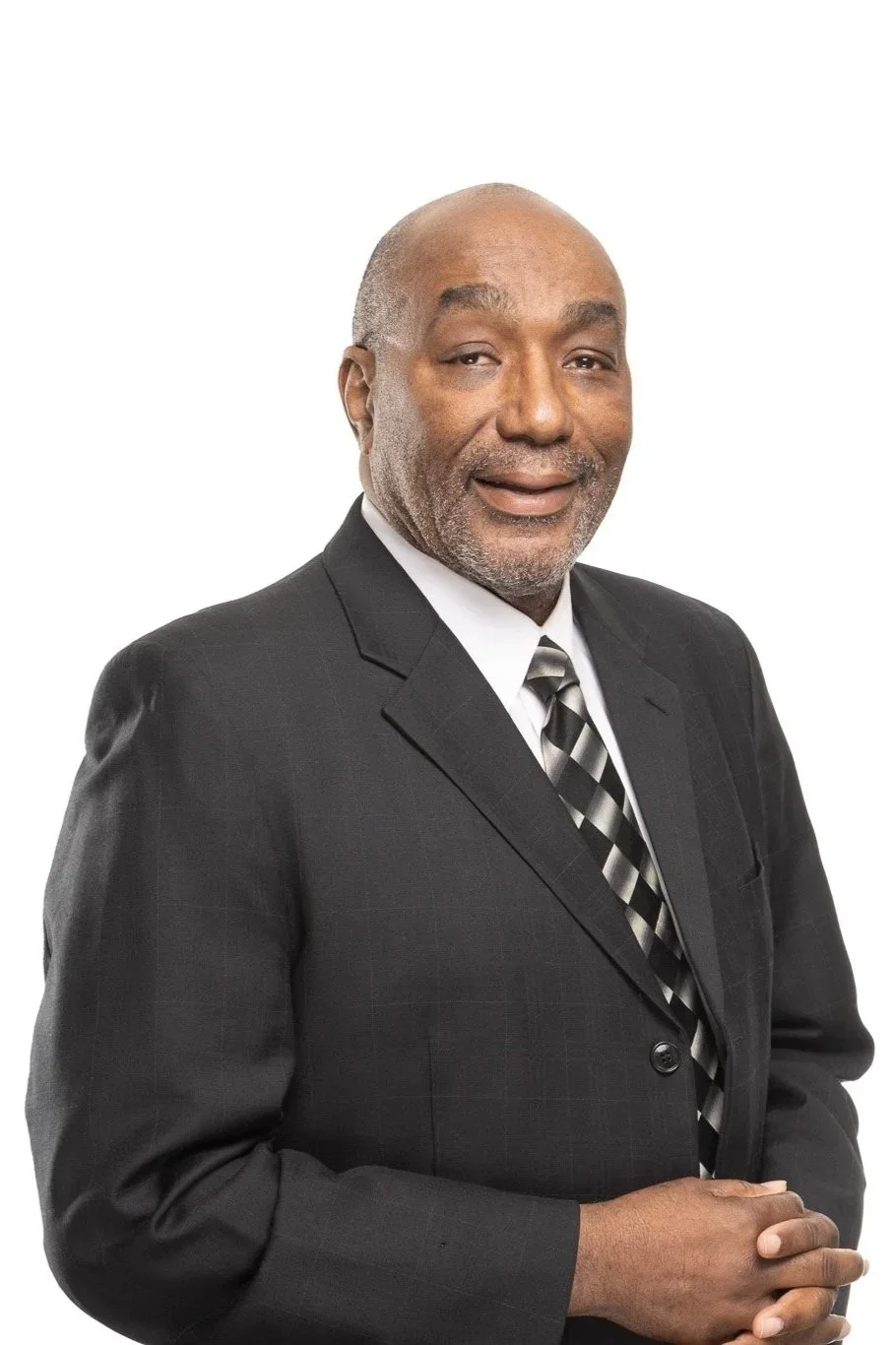 A middle-aged African American man dressed in a dark suit, white shirt, and striped tie, standing against a plain white background.