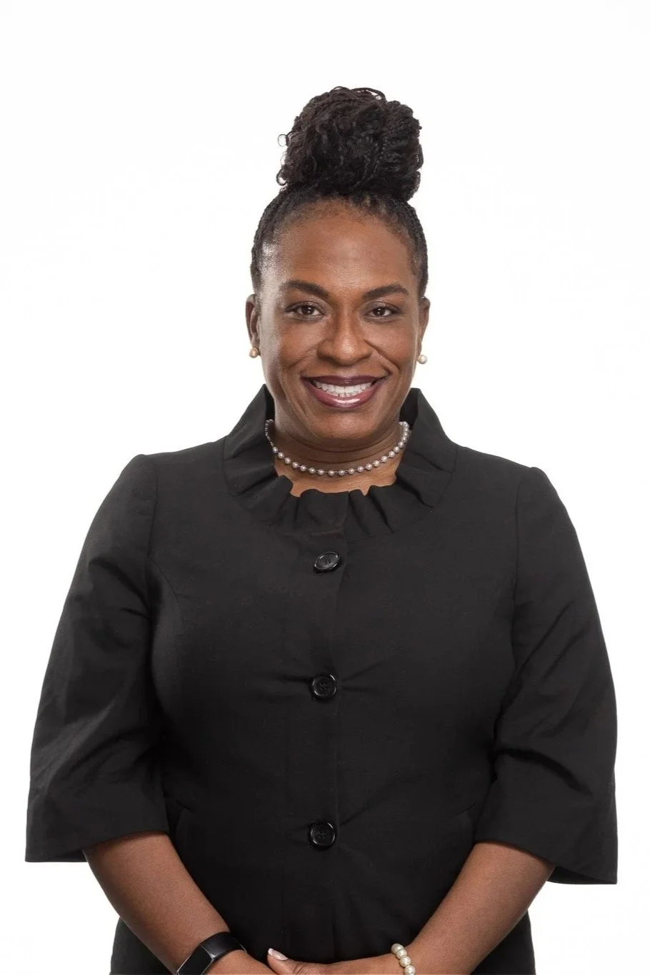 Portrait of an African American woman smiling in a black dress with pearl jewelry, against a white background.