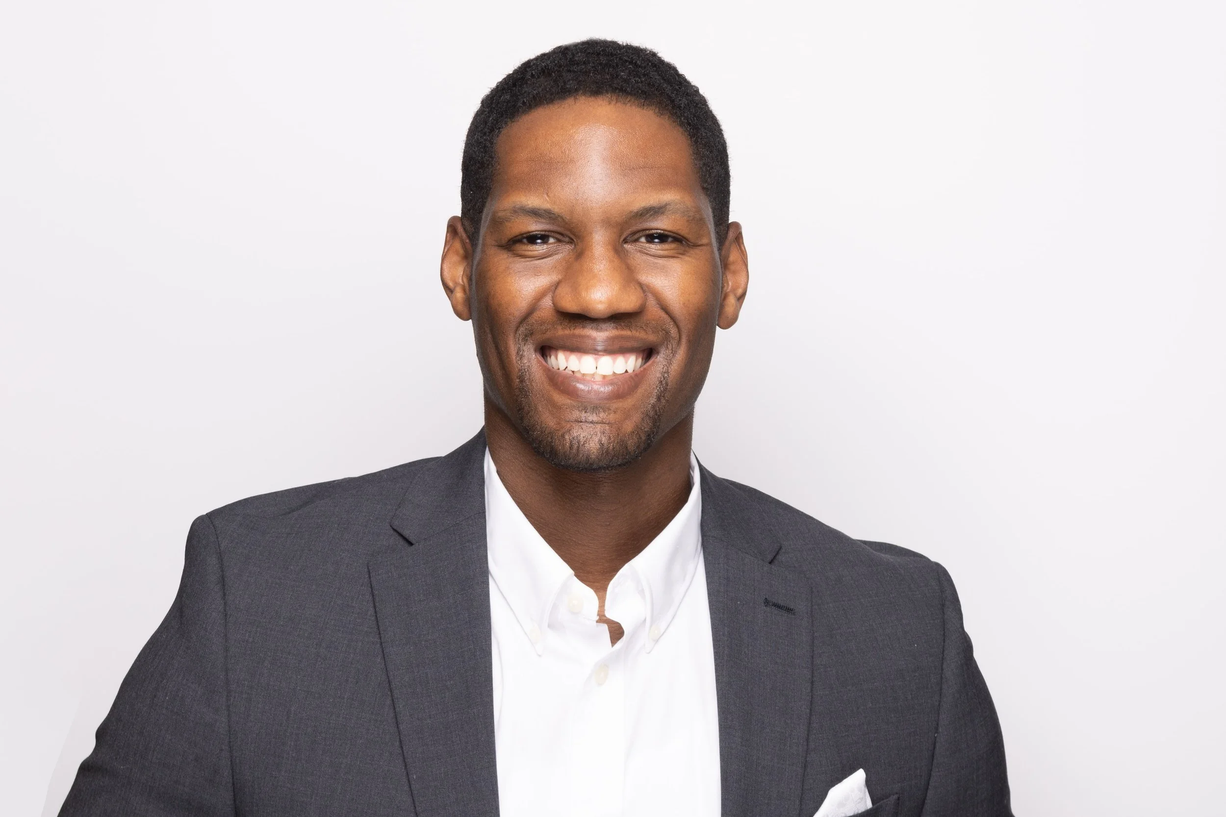 Portrait of a smiling African American man wearing a gray suit jacket and white dress shirt against a white background.