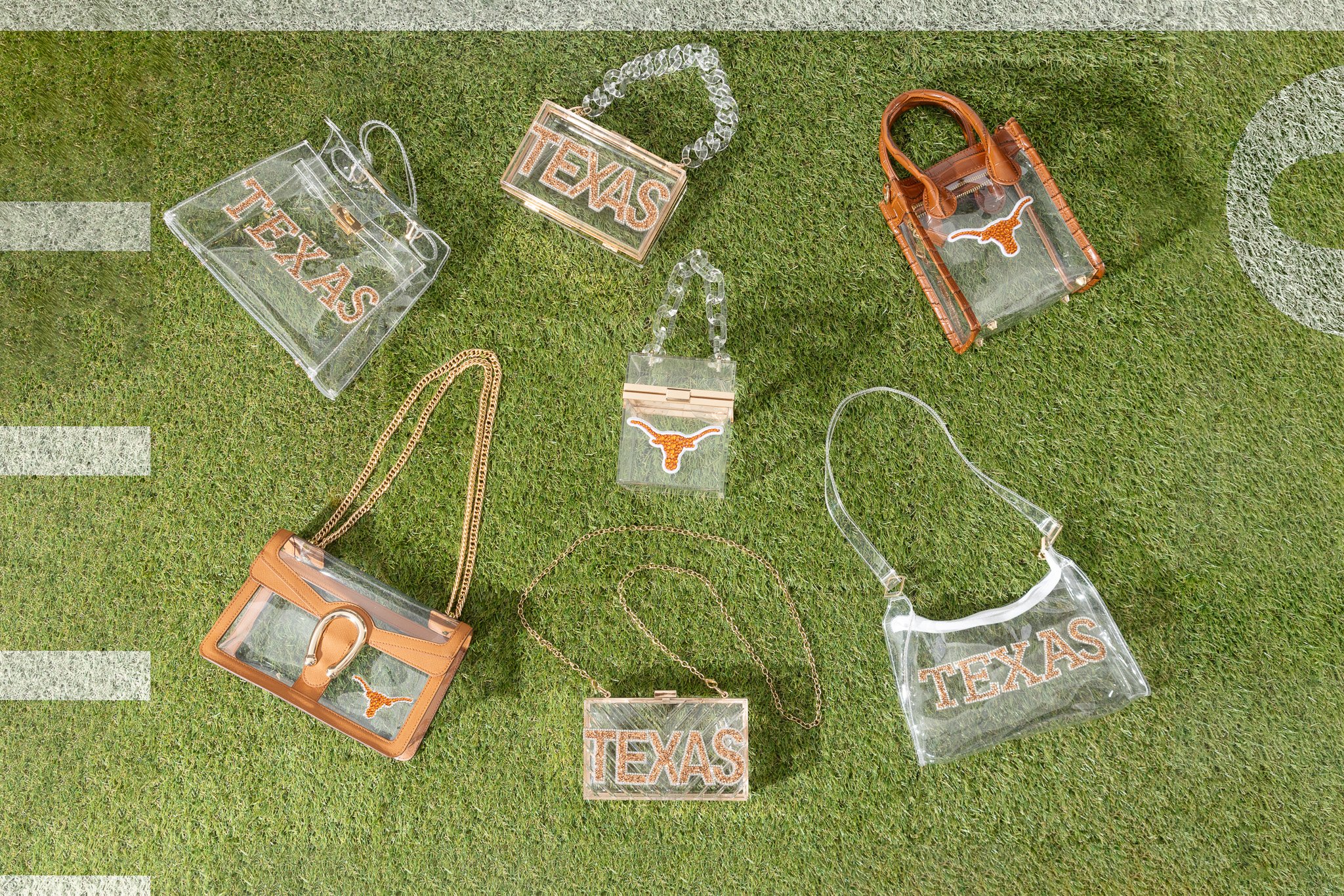 Various Texas-themed handbags, jewelry, and accessories with clear acrylic and orange accents, laid out on grass.