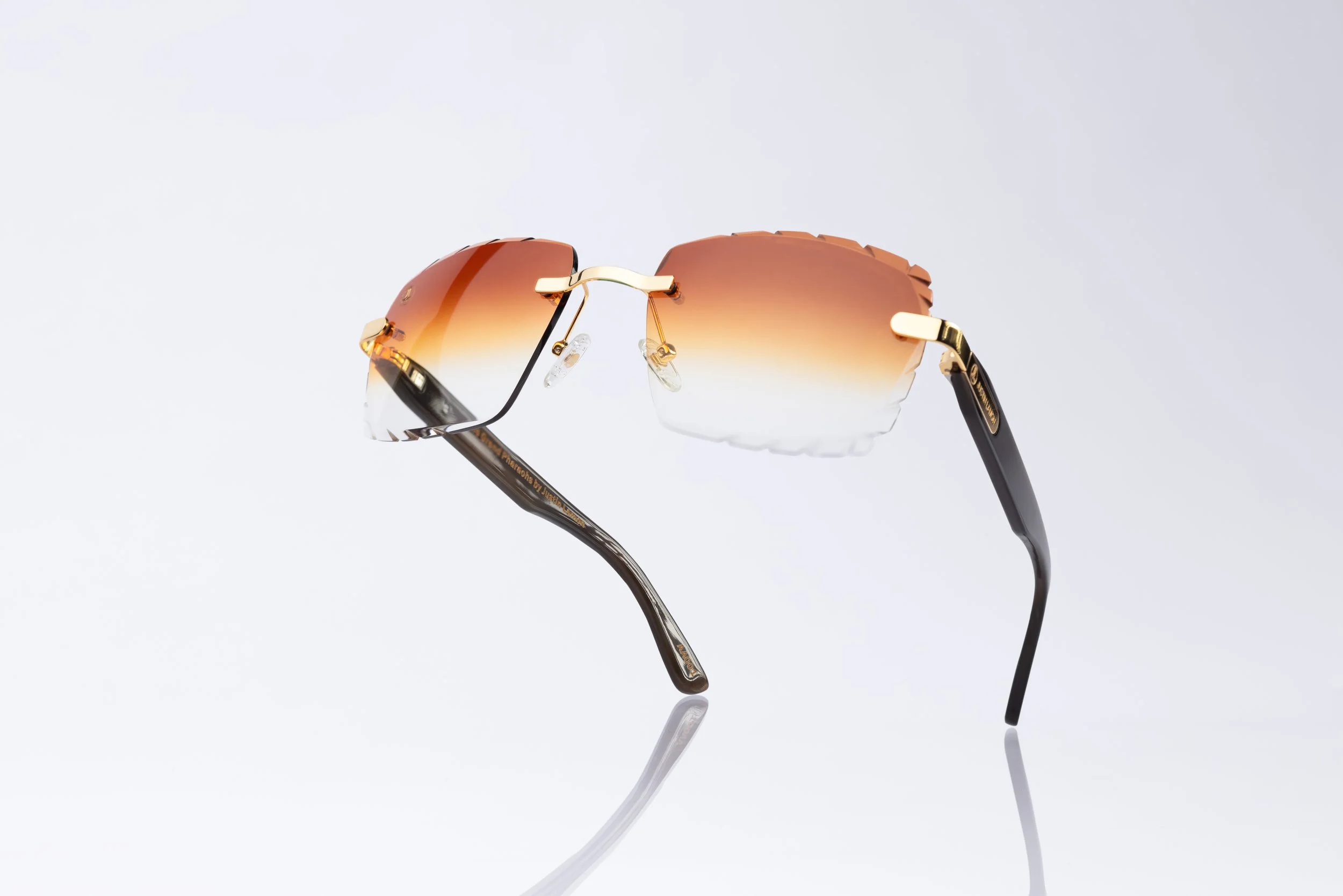 Pair of stylish sunglasses with gradient orange lenses and black and gold frames on a white background.