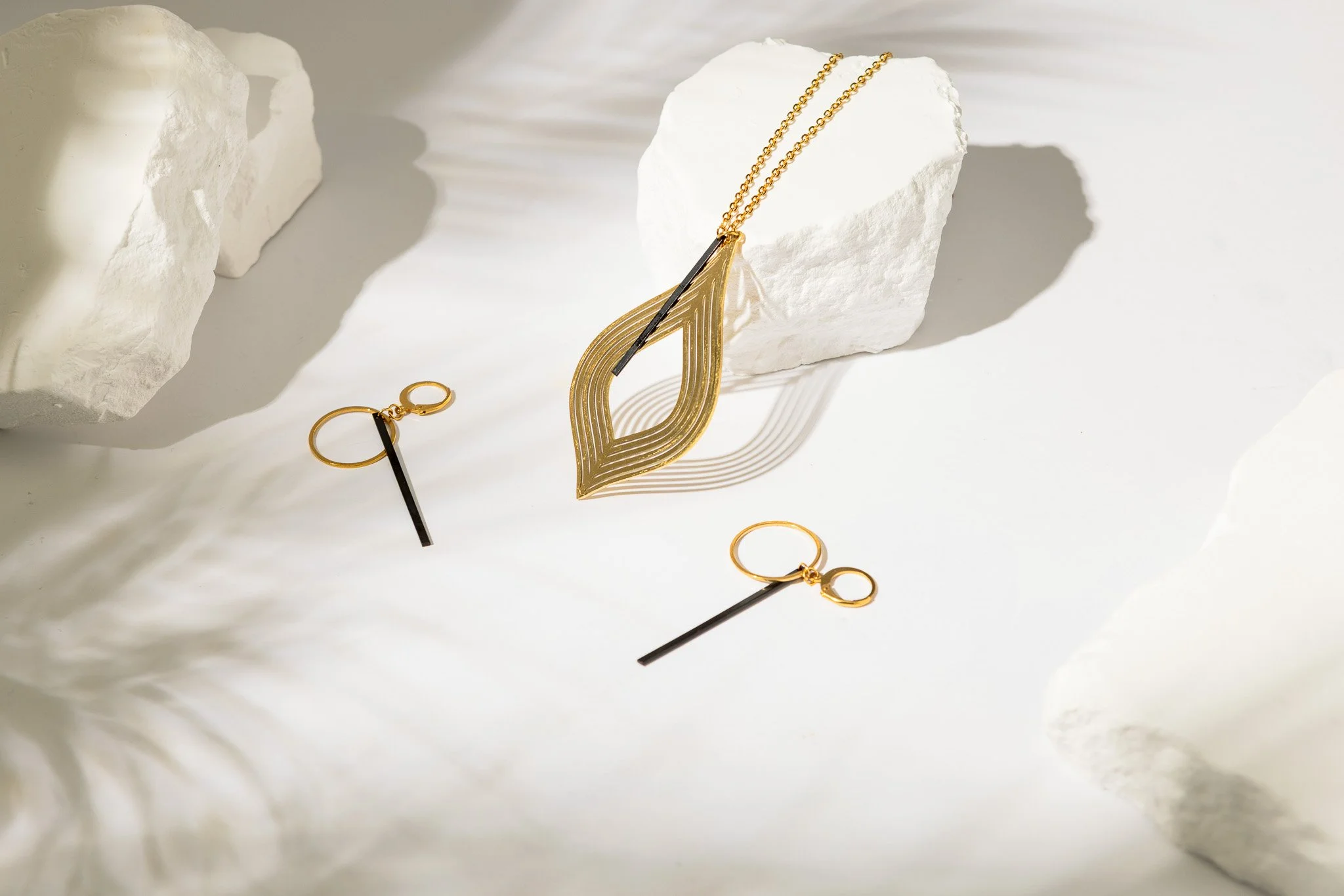 Gold jewelry including a necklace, earrings, and a bracelet displayed on white rocky surfaces.