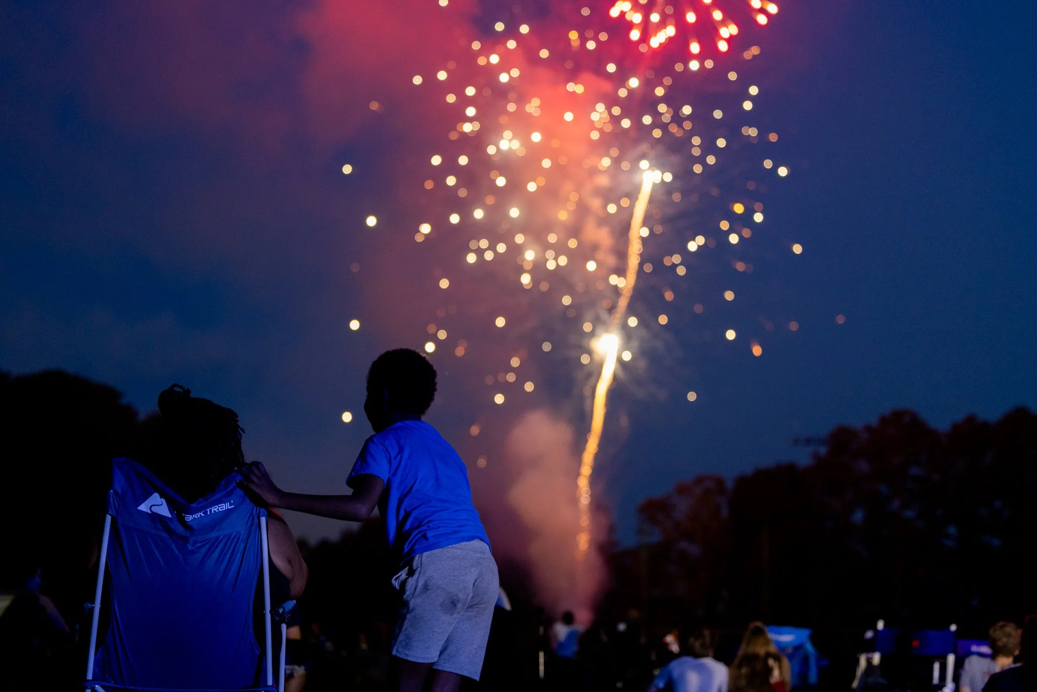 People watching fireworks in the night sky, silhouette of children in the foreground.