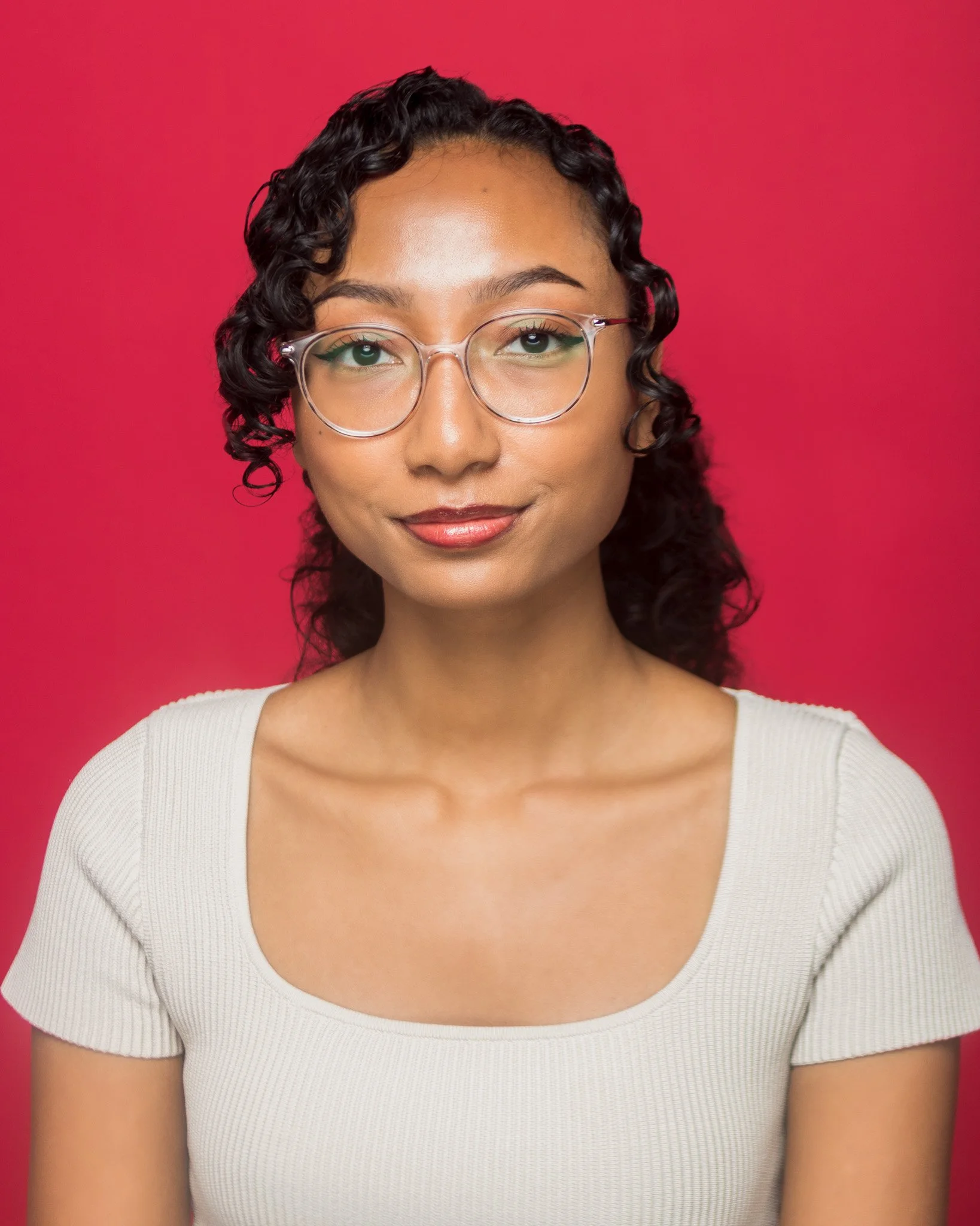 Close-up of a woman's face with glasses, smiling, against a pink background.