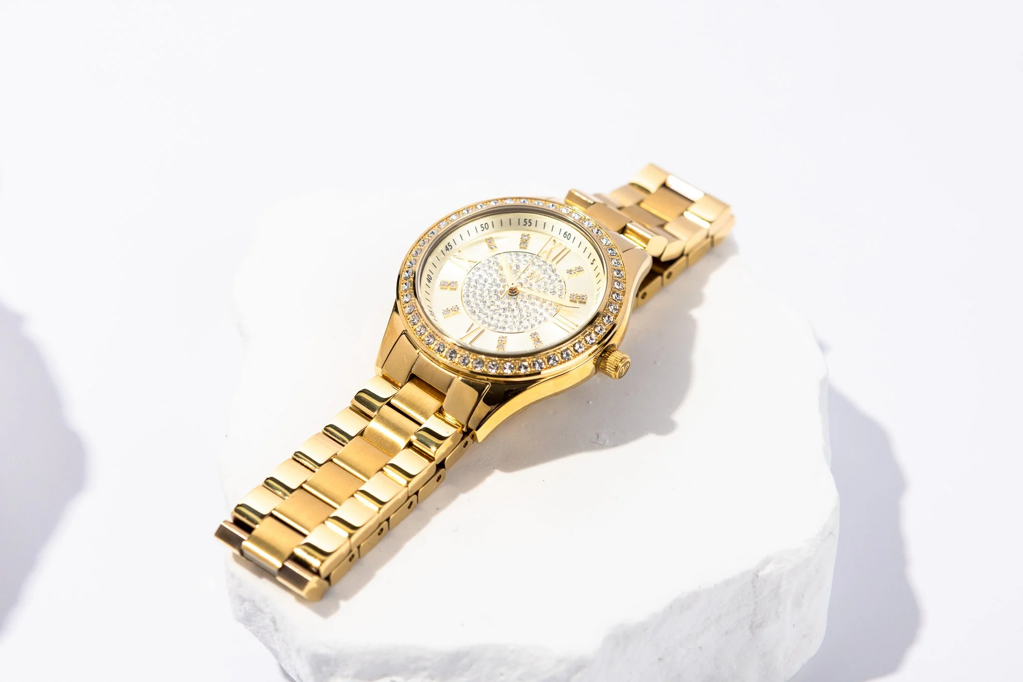 A gold wristwatch with a diamond-studded bezel and dial, placed on a piece of white marble.