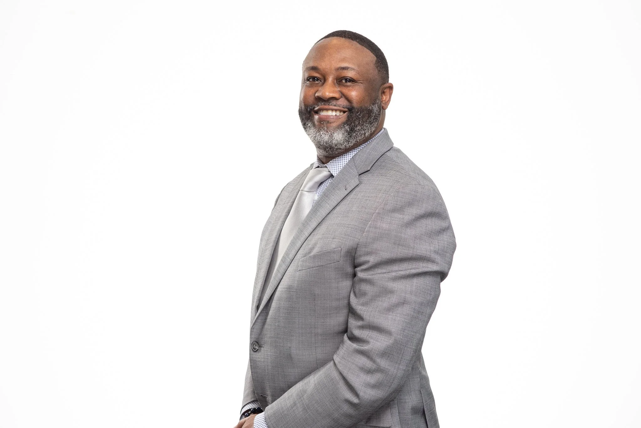 A man in a gray suit smiling, standing against a white background.