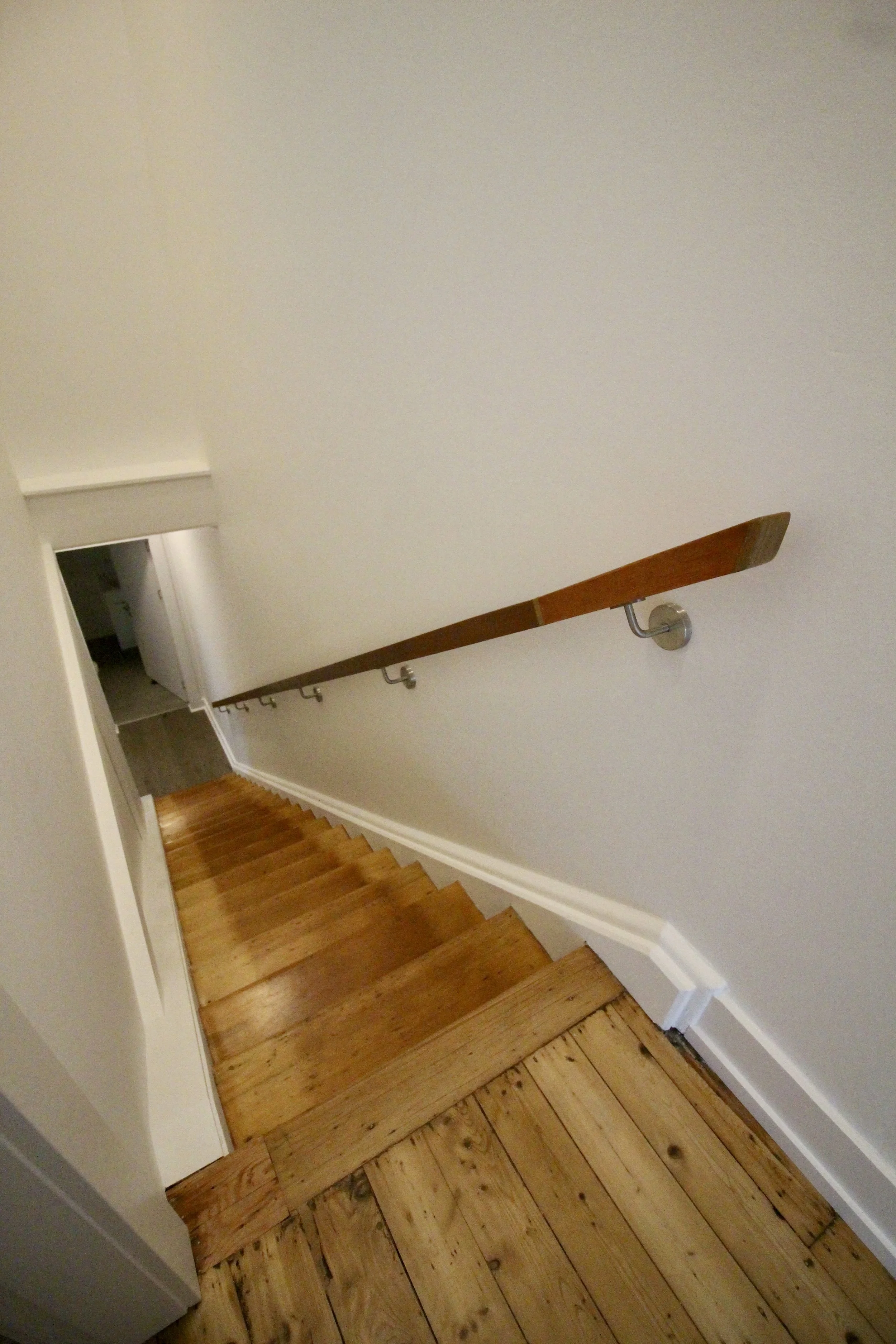 Wooden staircase with a curved handrail and white walls.