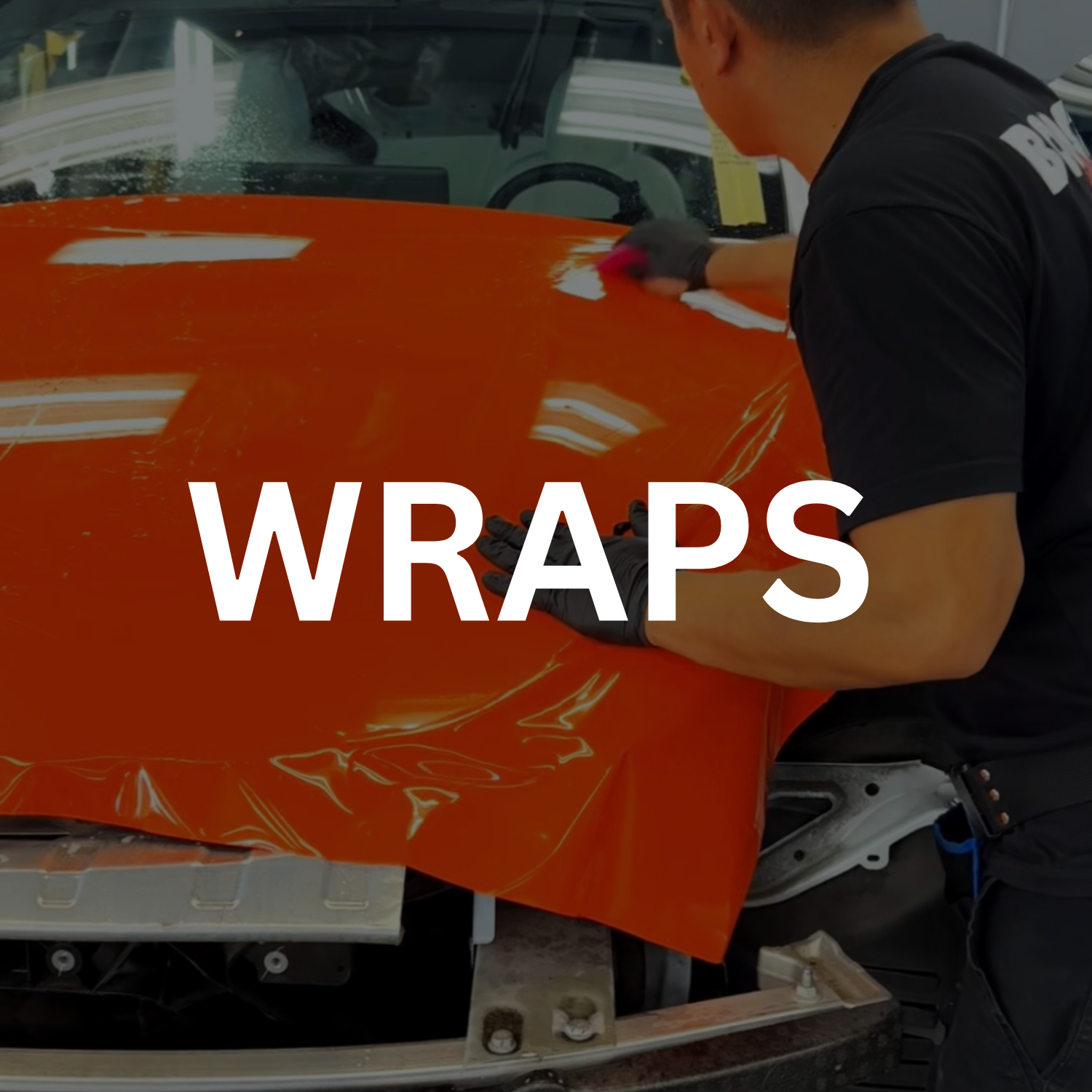A person applying orange wrap to the hood of a car.