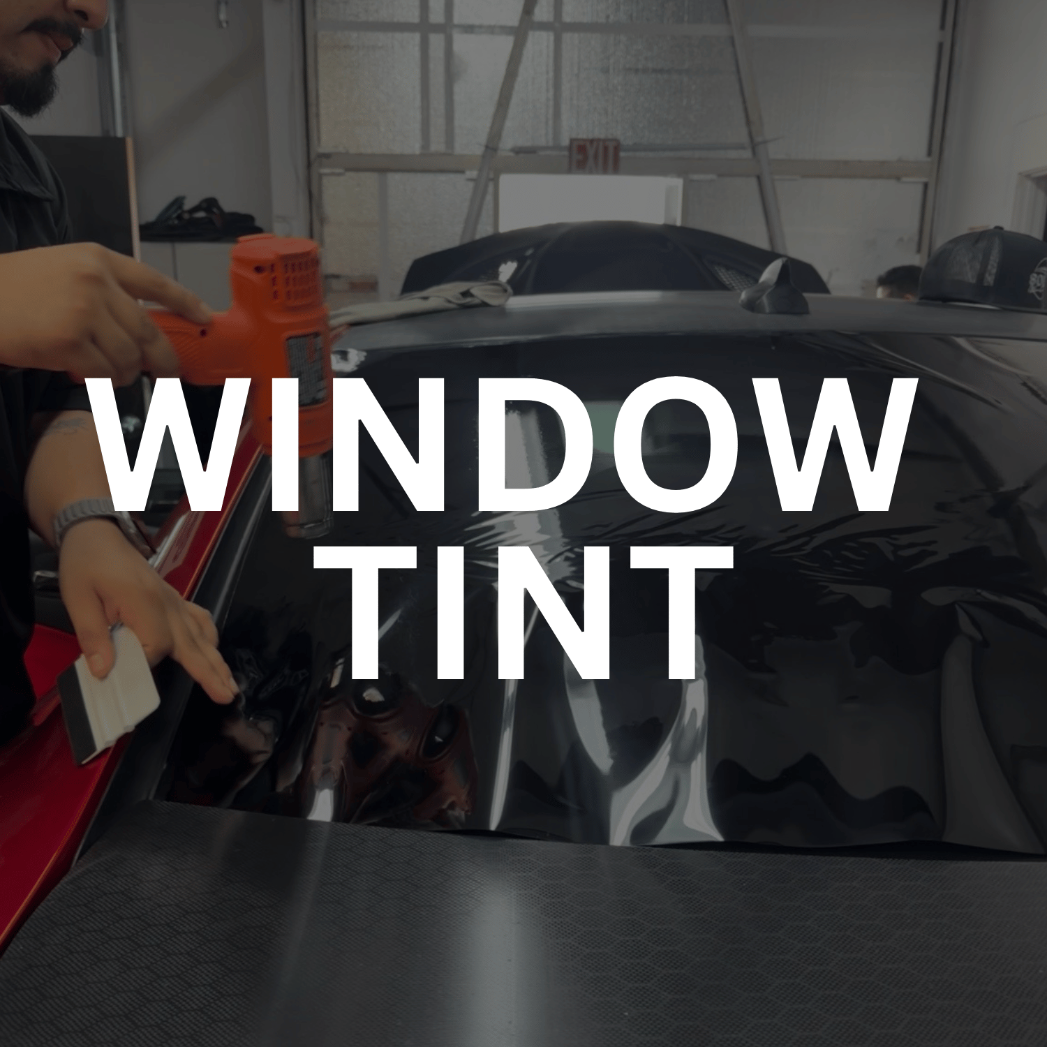 Person applying window tint film to a car windshield in a garage or workshop.