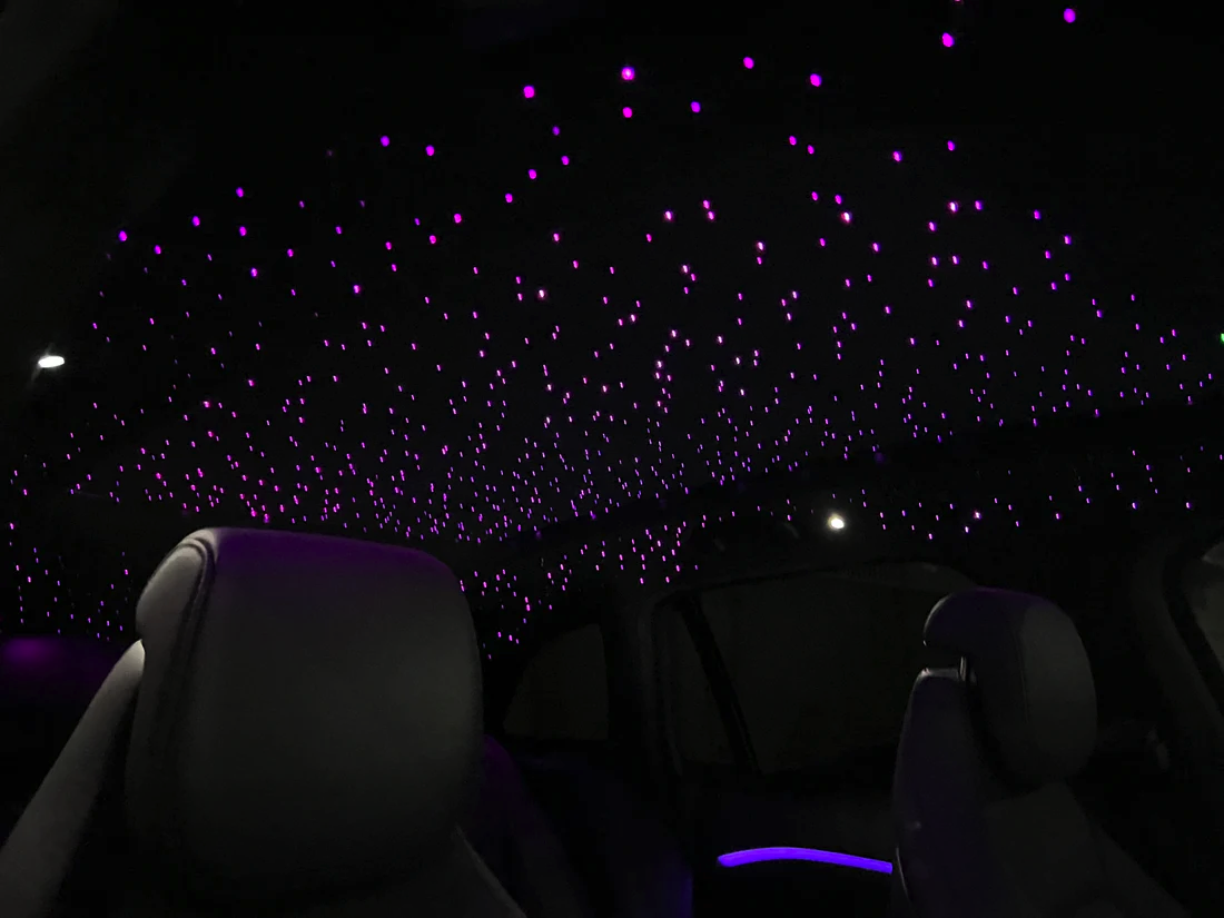 Interior of a car with a ceiling decorated with purple LED star-like lights.