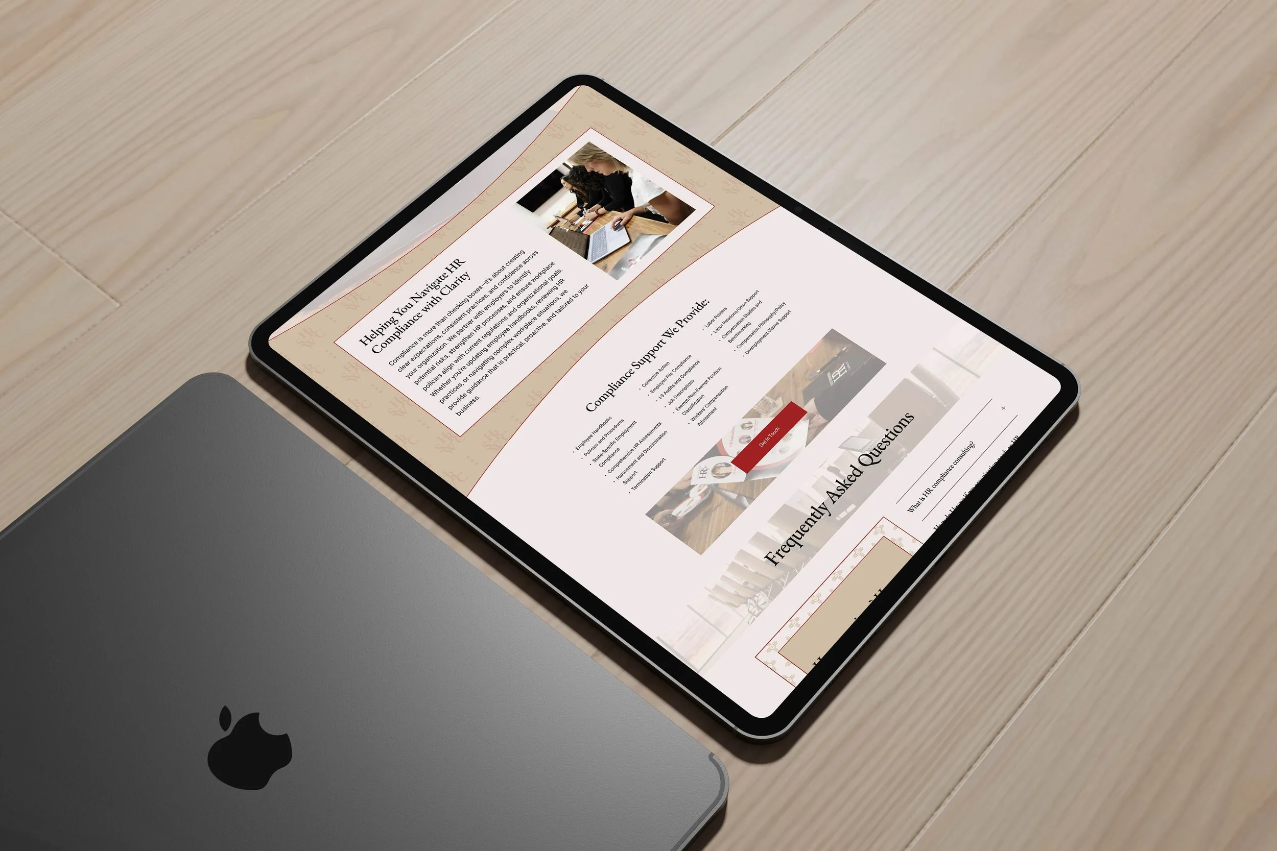 An iPad displaying a website about HR compliance, with a MacBook partly visible underneath on a wooden surface.