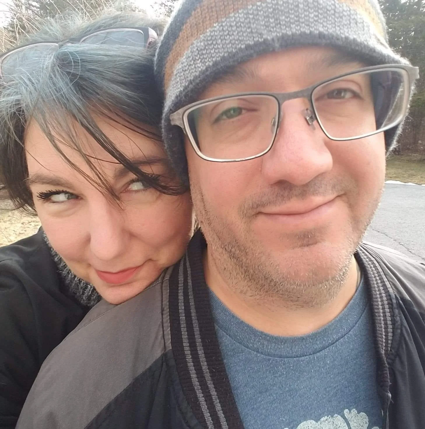 A bespectacled man who has an impish woman looking over his right shoulder with a smirk on her face.
