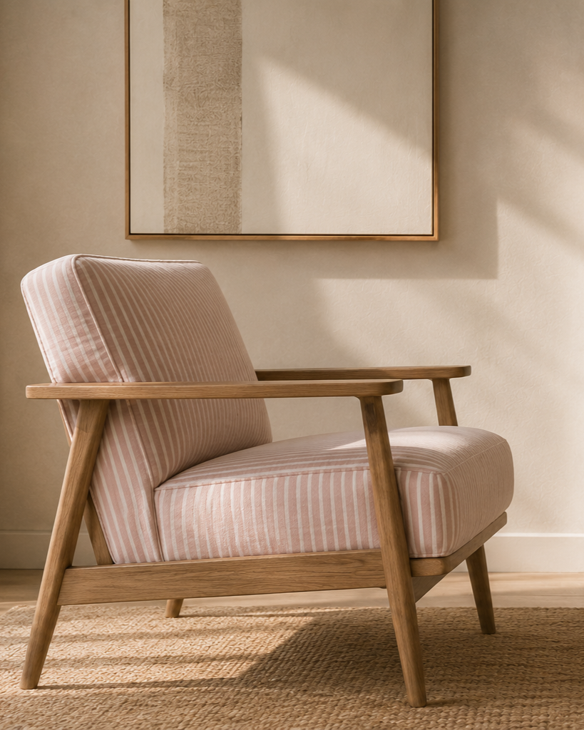 A pink-striped armchair with wooden armrests and legs placed on a woven rug in front of a beige wall with a framed abstract art piece. Openness. Calmness. Figuring out next steps. Setting and reaching goals.