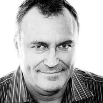 Black and white photo of a man with short hair, wearing a striped shirt, smiling slightly.