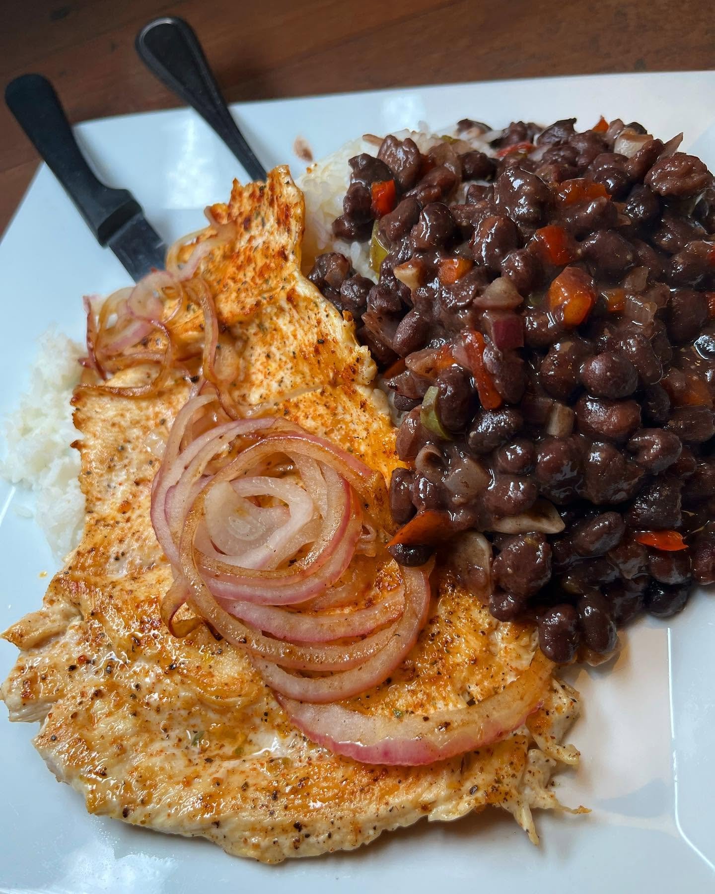 A white plate with grilled fish topped with cooked onions, served with mashed potatoes and a large portion of beef stew with vegetables.