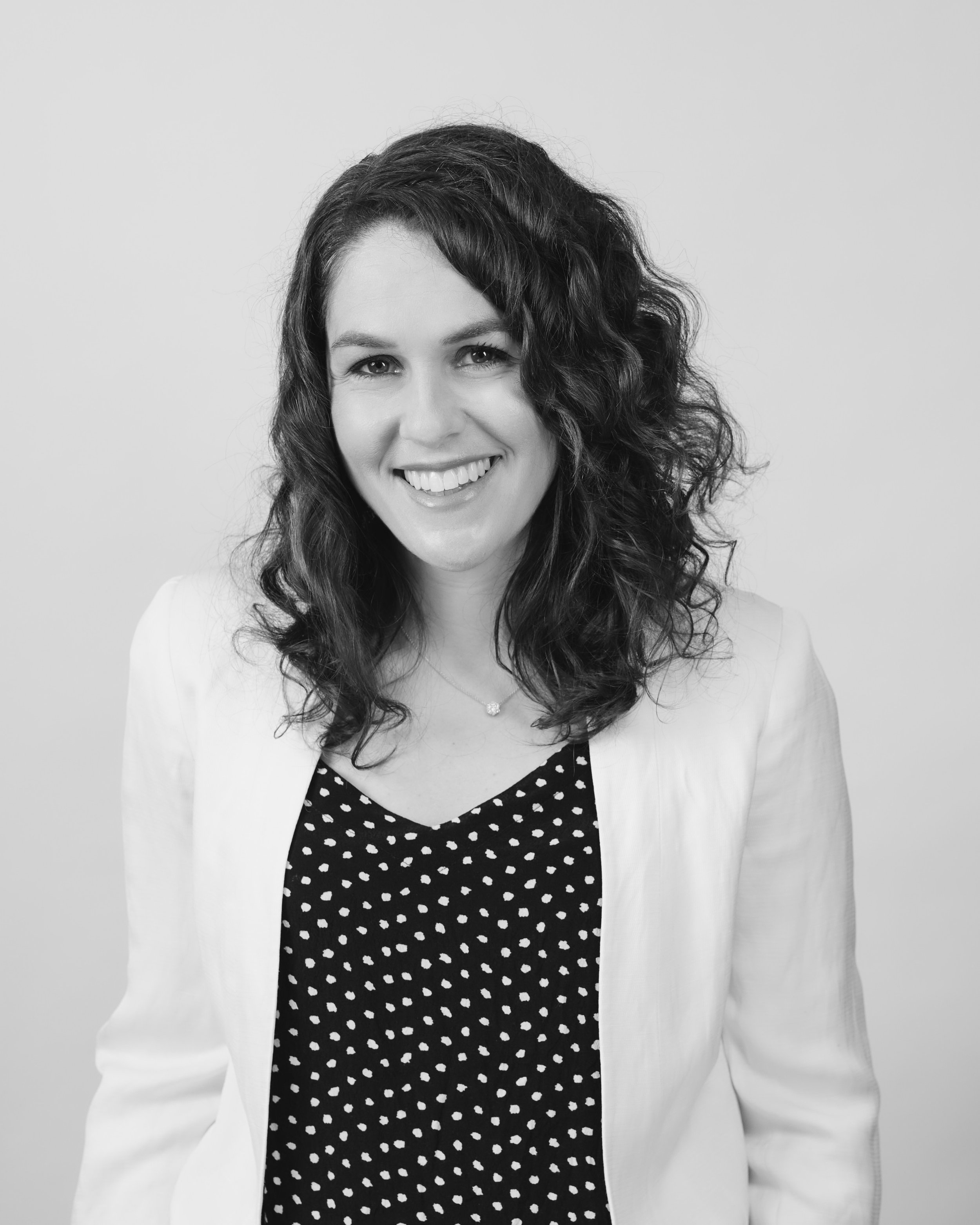 Laura Peressini, Managing Partner at Oreana Advice Partners wearing a light-colored blazer over a polka-dot top, and a delicate necklace, standing against a plain background.