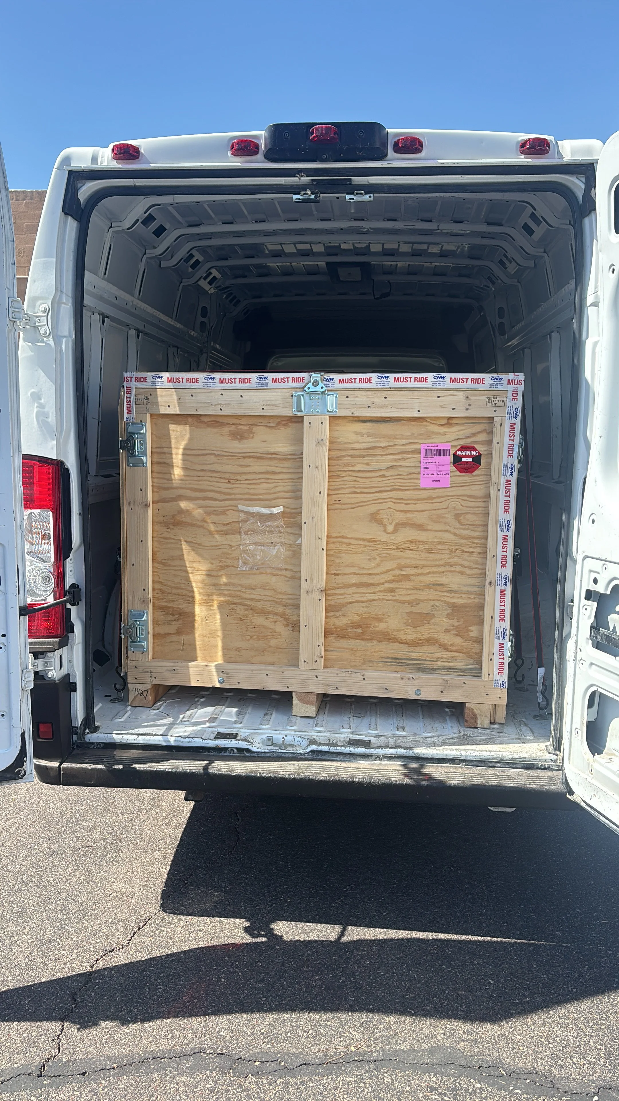 Open van with a large wooden crate inside, parked on asphalt with blue sky overhead.