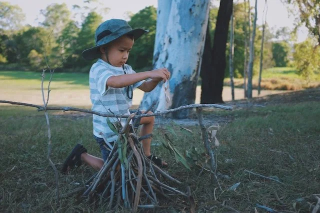 A young boy building a campfire with sticks in a park.