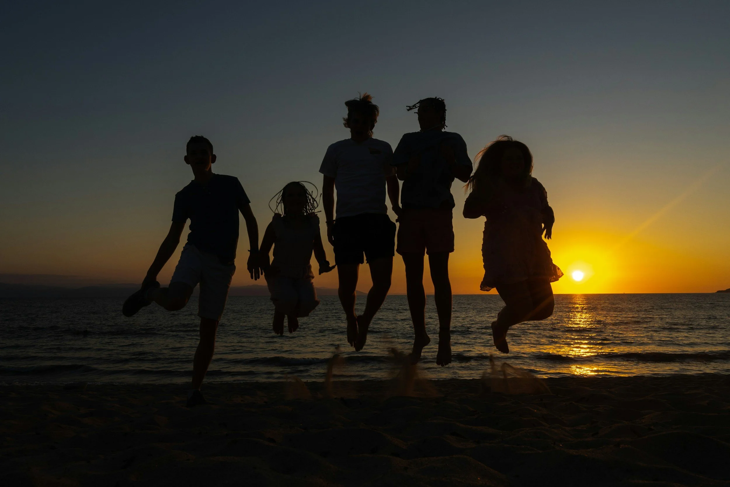Silhouetted children jumping on a beach at sunset.