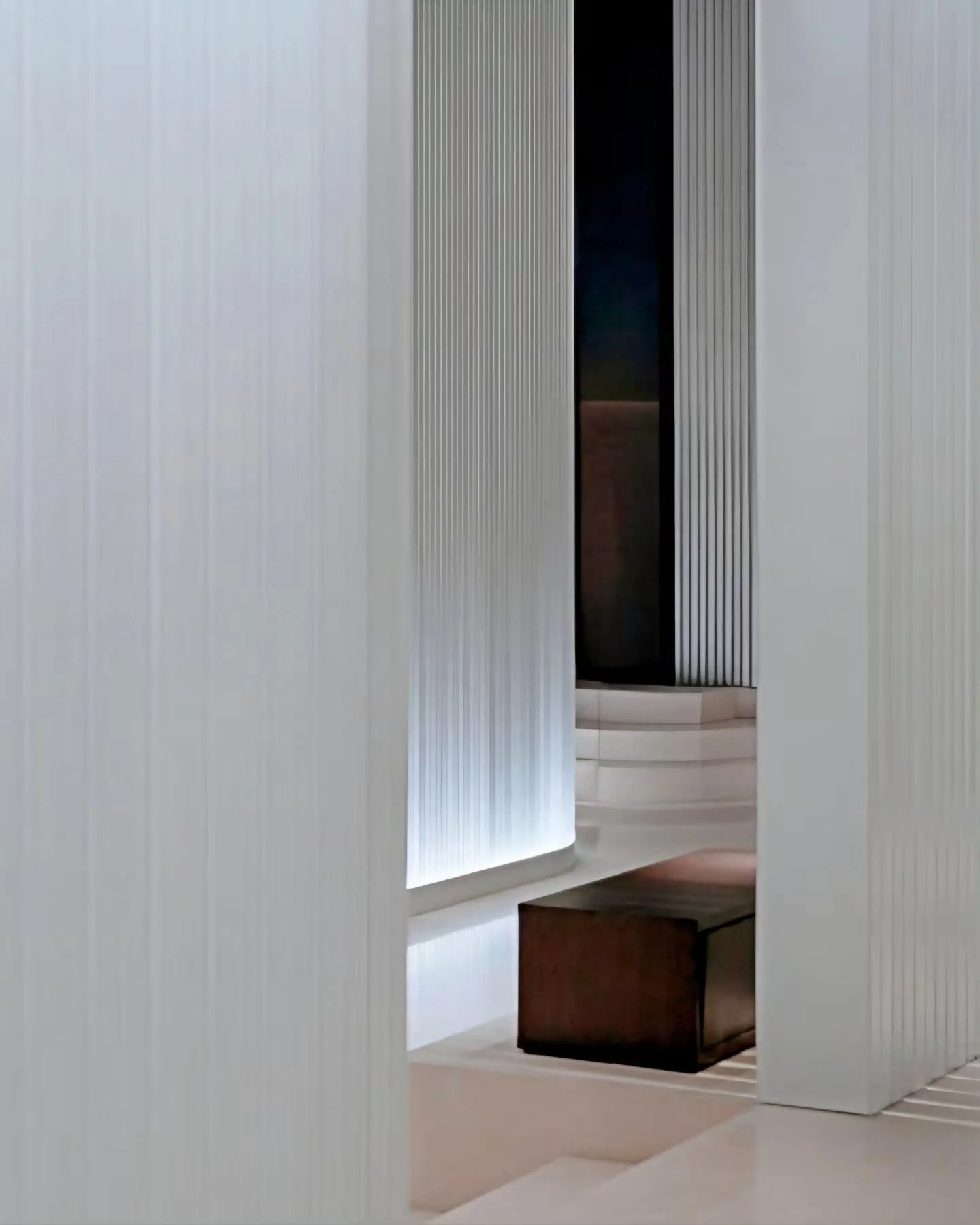 Recessed halo lighting grazes translucent fluted screens&mdash;casting delicate linear shadows across stepped stone plinths and a solitary dark timber block. 

​Interior Design by MQ Studio.

​The Corridor at @thepuxuanhotelandspa

​Read the full fea