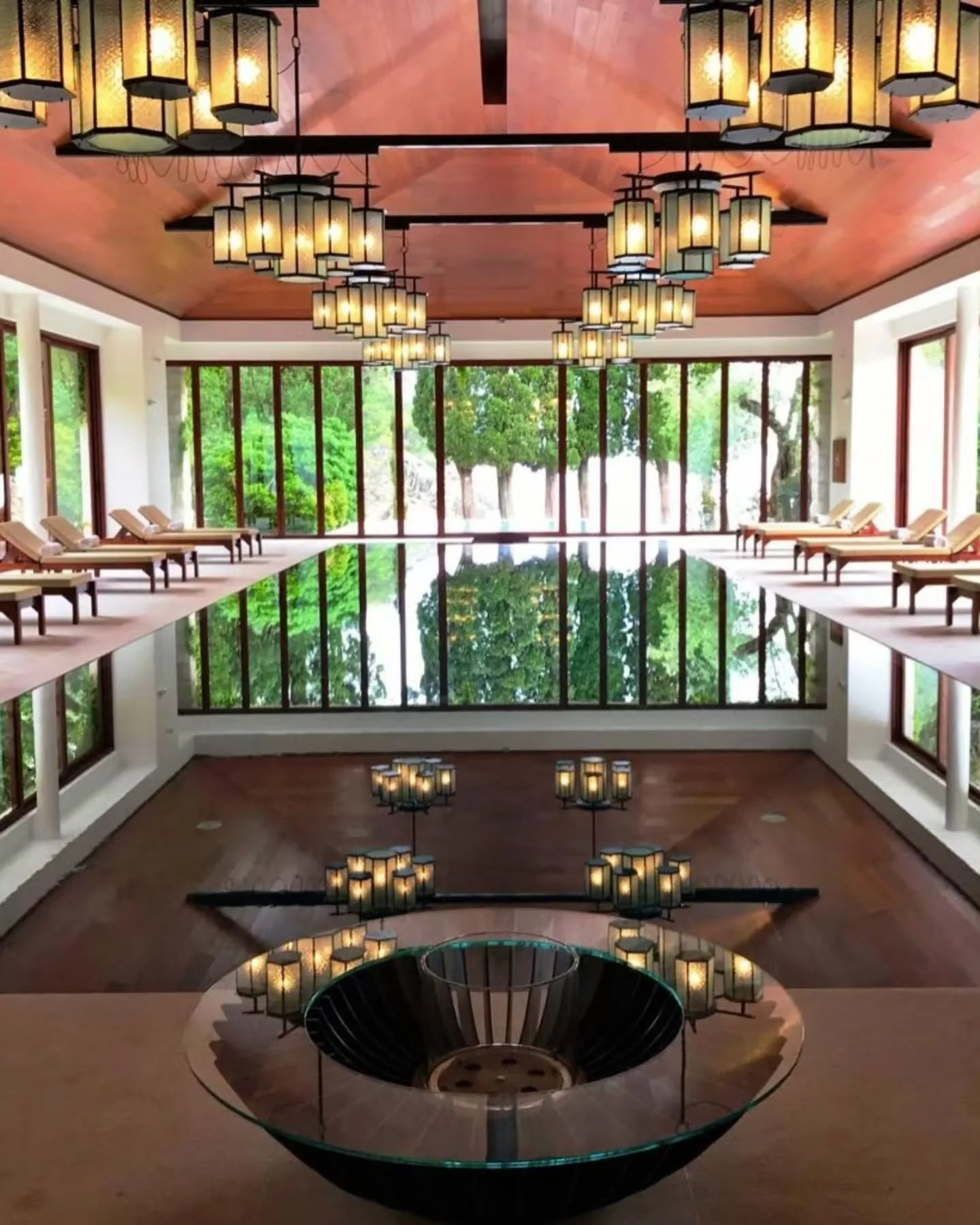 Tiered brass lanterns mirror along dark reflecting waters, accentuating Jean-Michel Gathy&rsquo;s structural discipline through warm timber paneling, aligned teak frames, and floor-to-ceiling glass fenestration.

​Interior Design by Jean-Michel Gathy