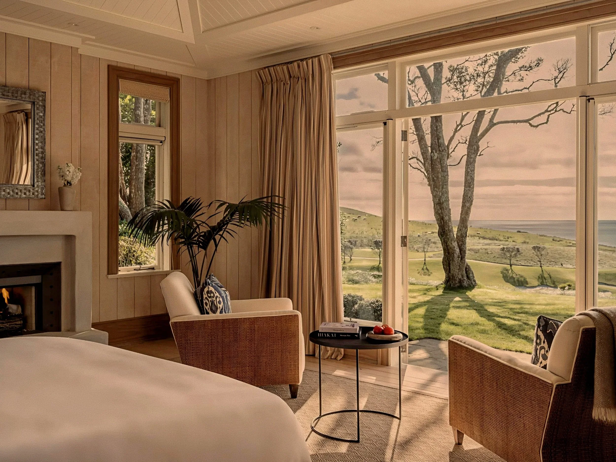 Oceanfront luxury suite bedroom with fireplace and Pacific views at Rosewood Kauri Cliffs, New Zealand.