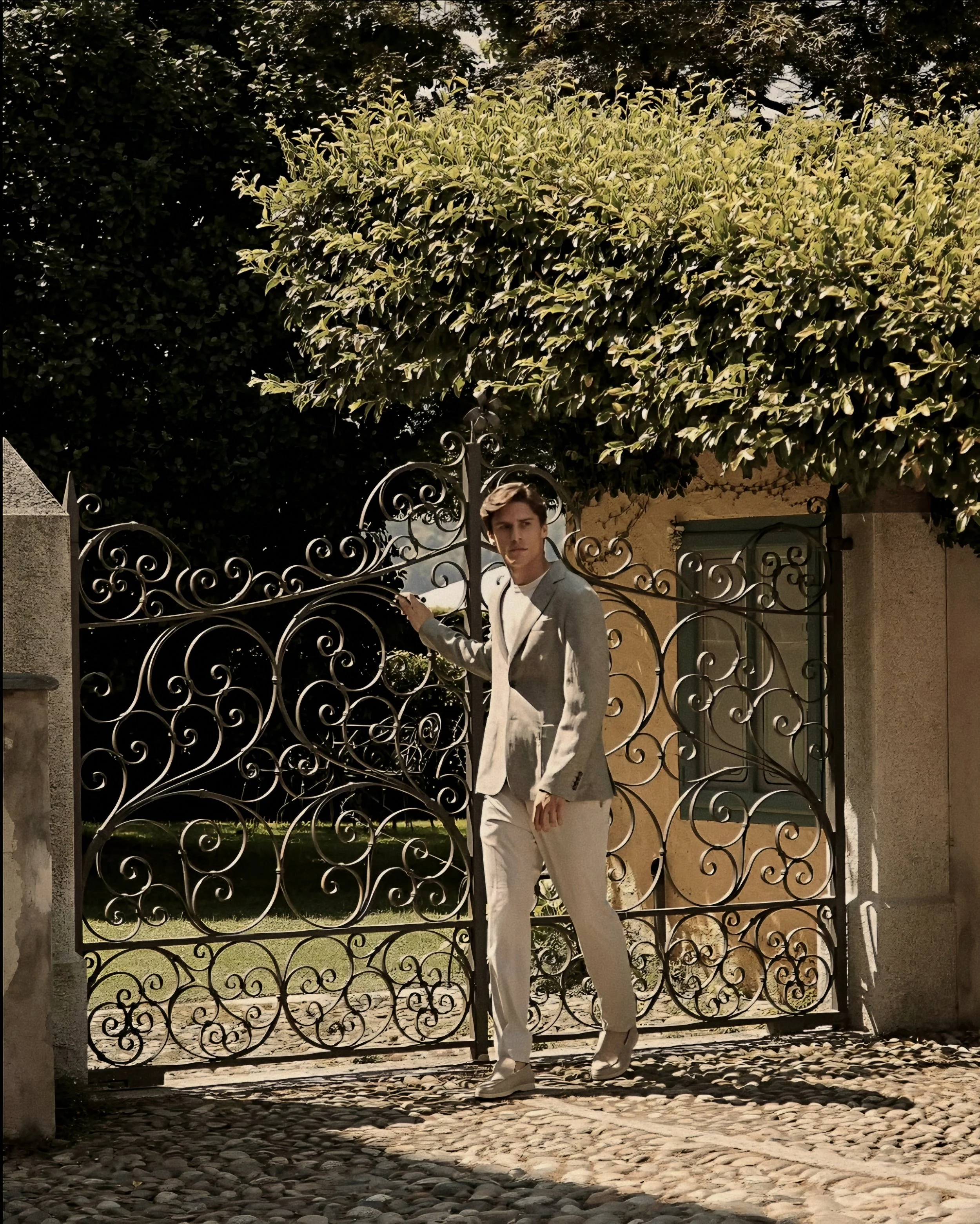 Monochromatic double-breasted suit tailoring by Lanificio Colombo framed by classical wrought-iron gates in Piedmont, Italy.