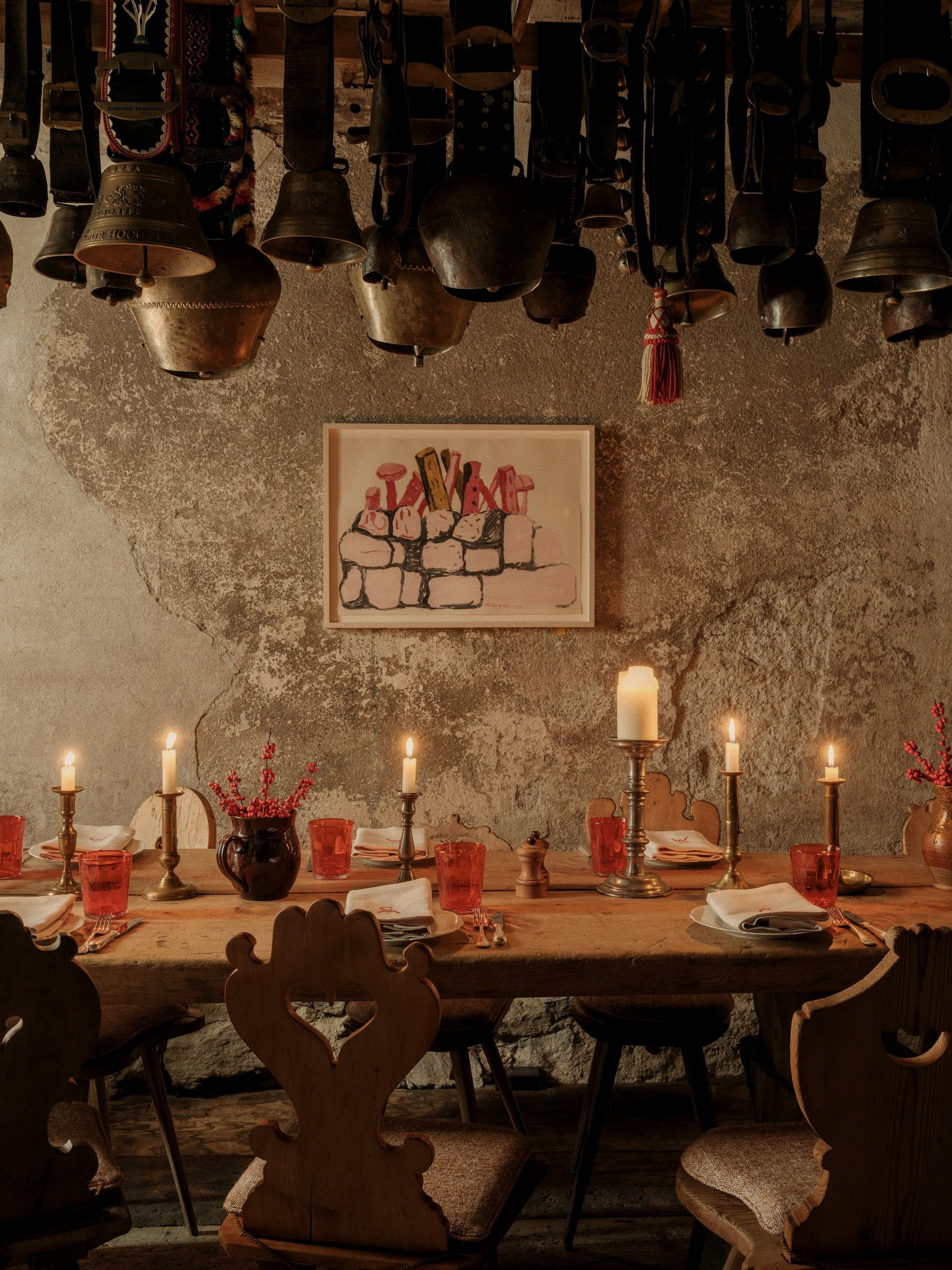 Atmospheric candlelit Alpine dining room set beneath antique cowbells at Chesa Marchetta in Switzerland.