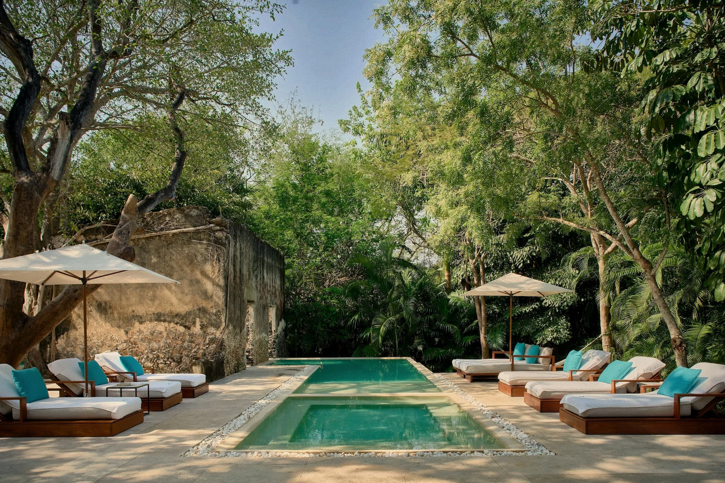 Teak sun loungers beside swimming pool and stone ruins at Hacienda Chablé Yucatán, Chocholá, Mexico.
