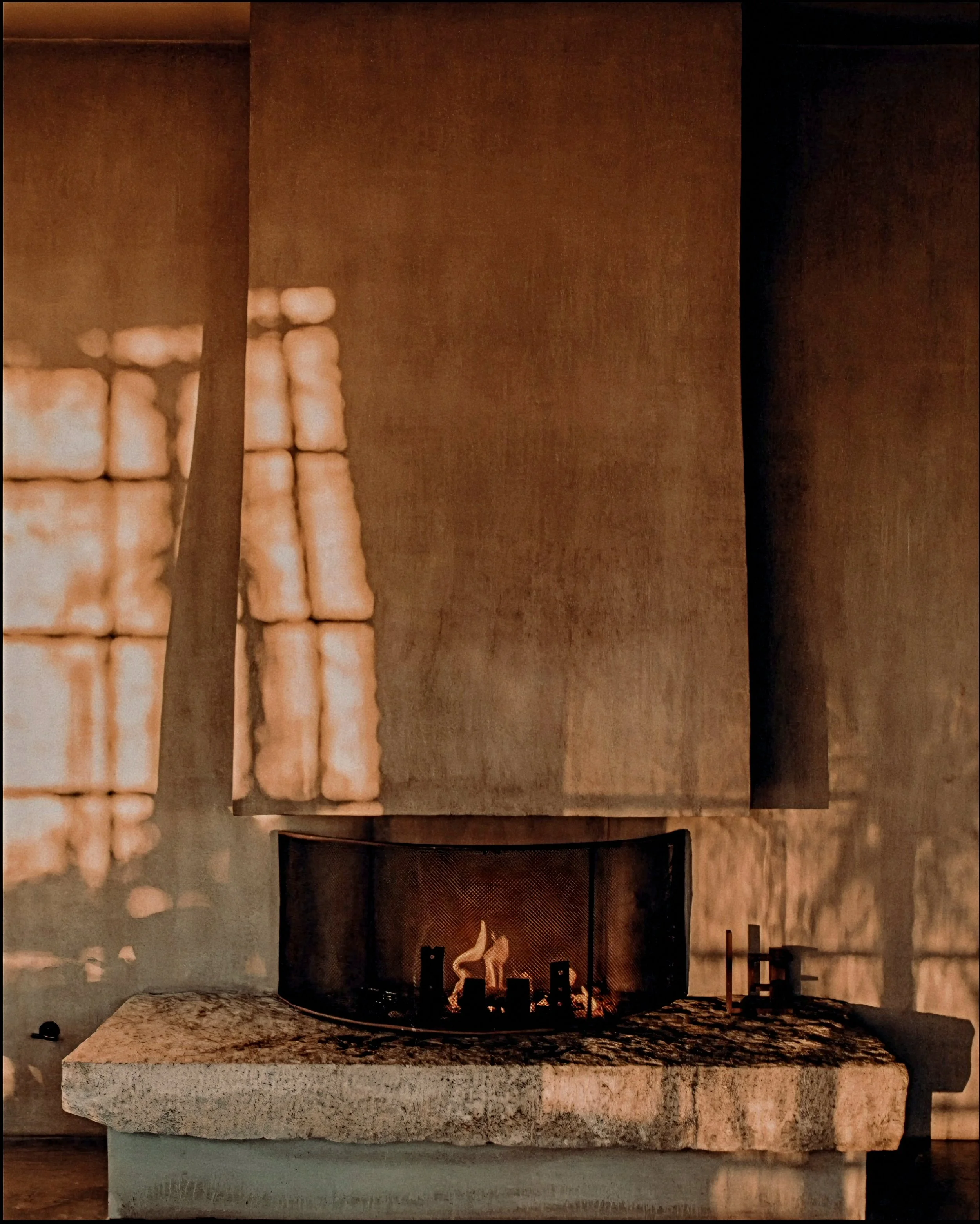 Monolithic carved stone hearth cast in soft firelight in the wabi-sabi TriBeCa penthouse, Manhattan.