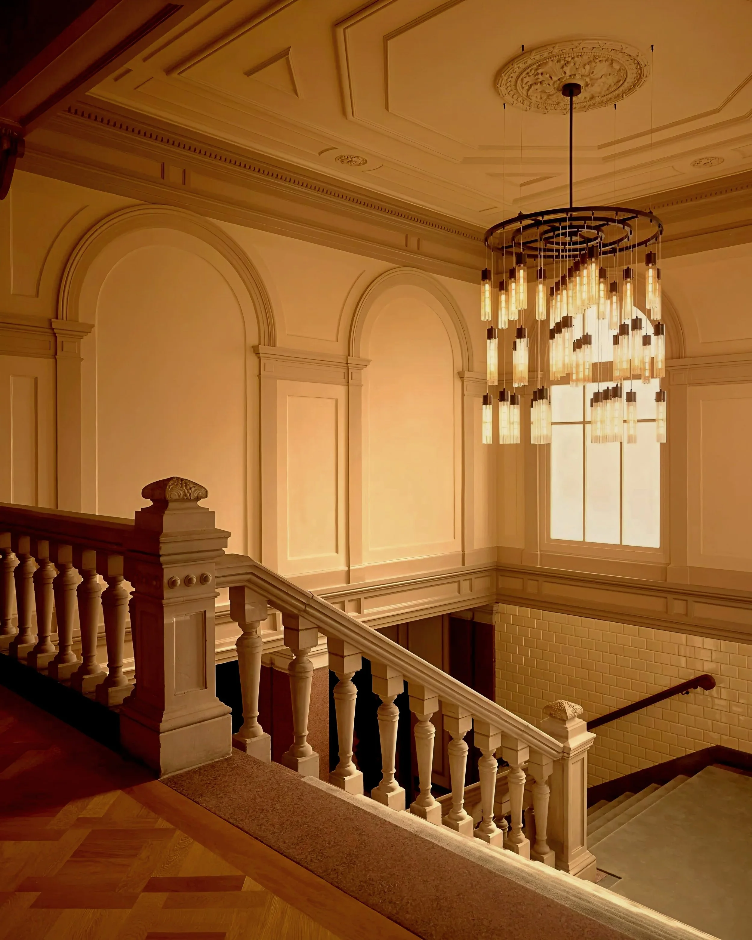A sweeping architectural staircase framed by classic arched wall paneling and a monumental, tiered circular chandelier—setting an atmosphere of ultra-luxury interior design and high-end living for the ROYAUME Magazine homepage.