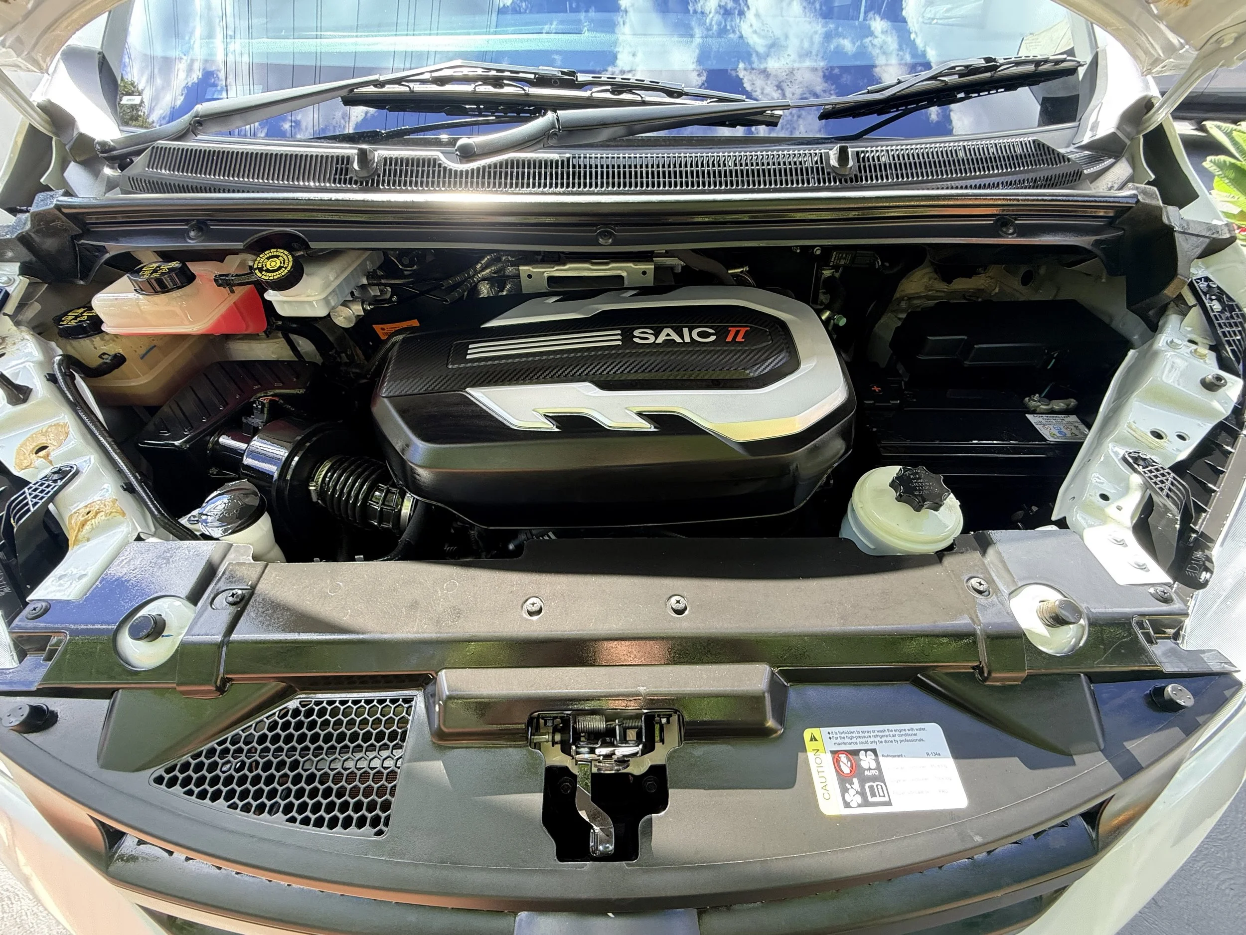 Under the hood of a car showing engine components, including a large cover with 'SAIC' and 't' logos.