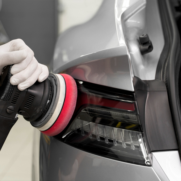 Person using a polishing machine with a red foam pad to polish the back of a silver car.
