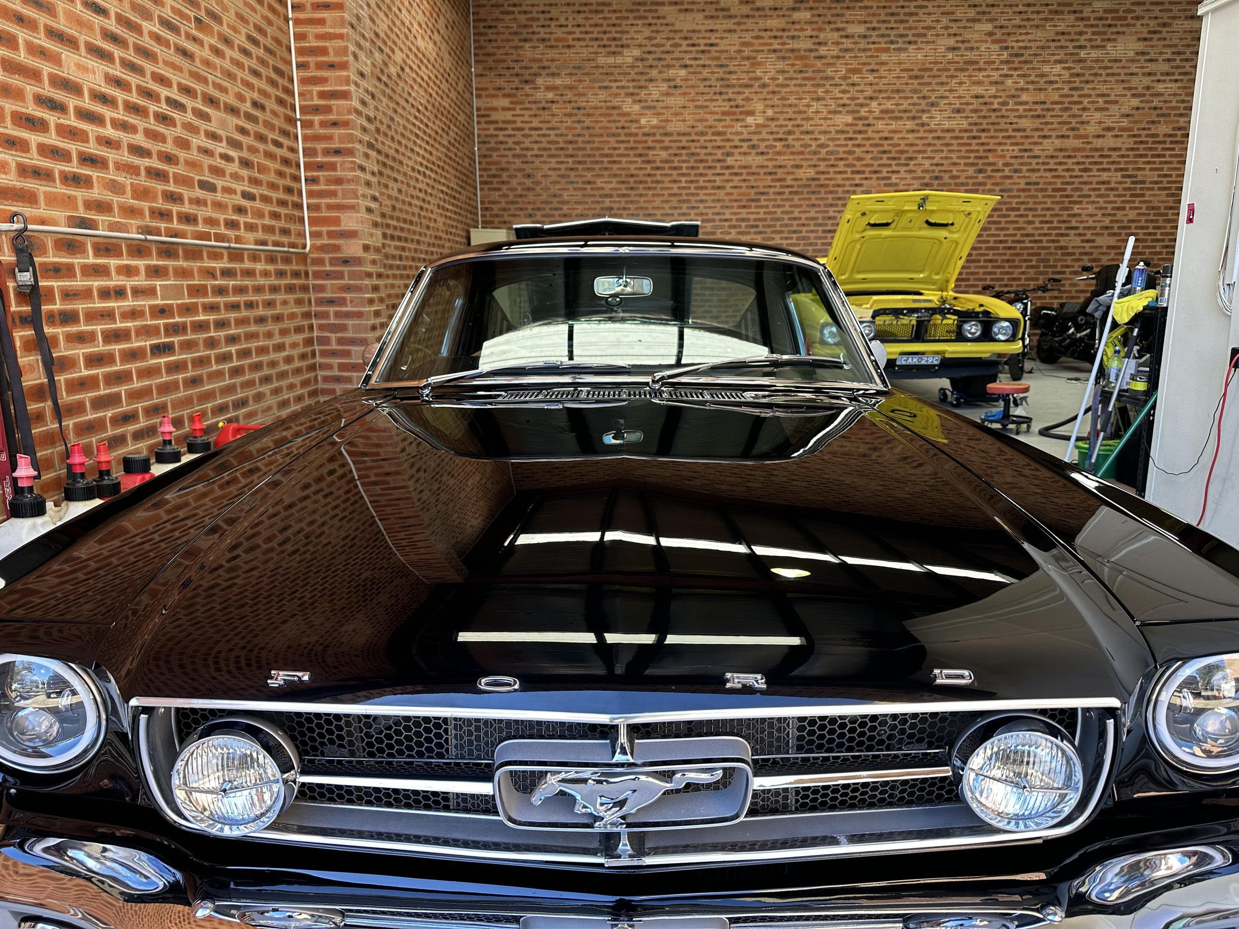 Front view of a black vintage Ford Mustang car parked inside a garage with red brick walls.