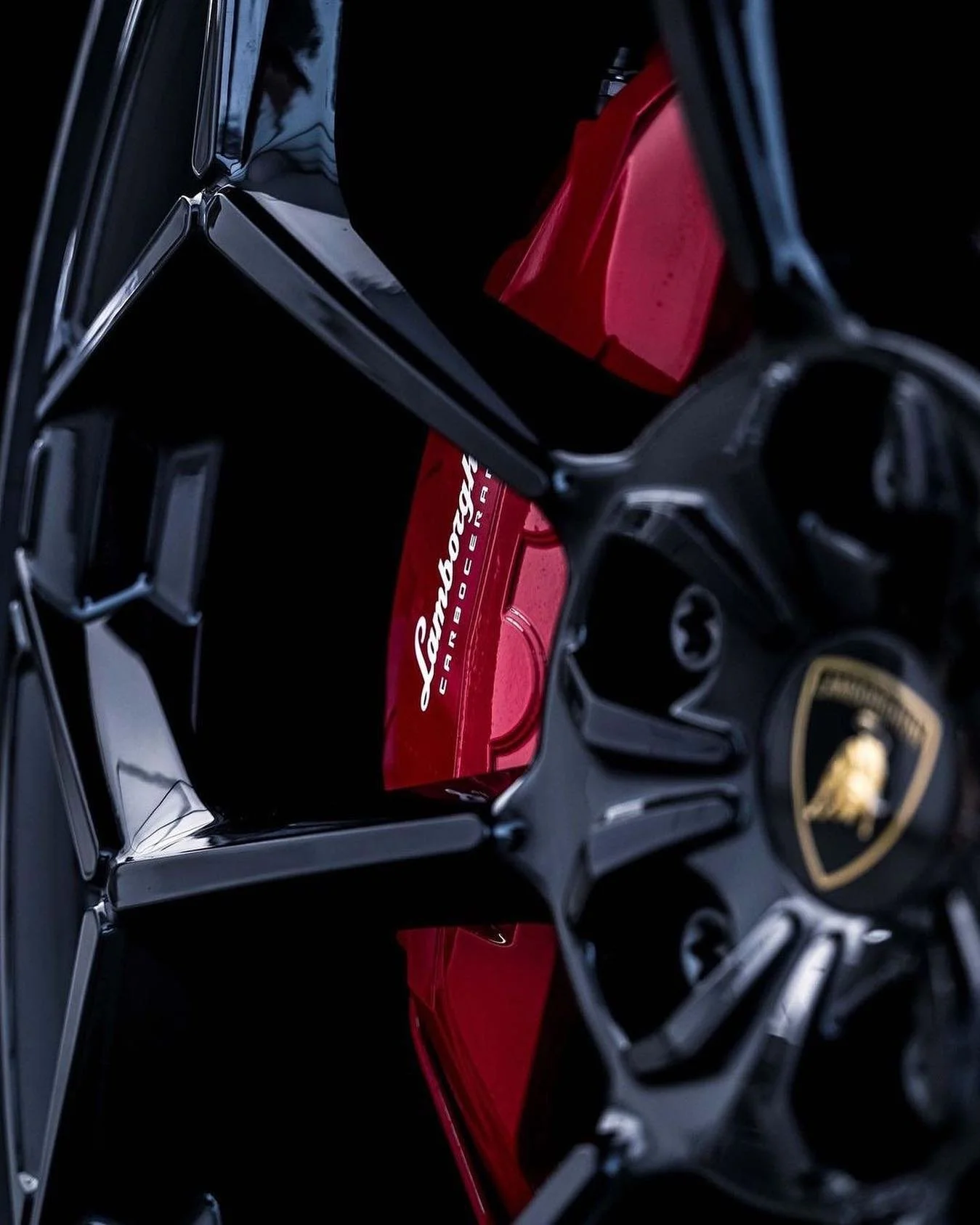Close-up of a luxury black car wheel with a Lamborghini logo at the center, featuring red Lamborghini-branded boxes inside the wheel.