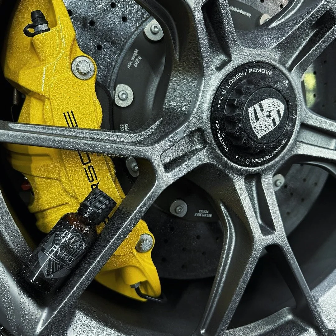 Close-up of a Porsche car wheel with a yellow brake caliper and a bottle of detailing spray on the rim.