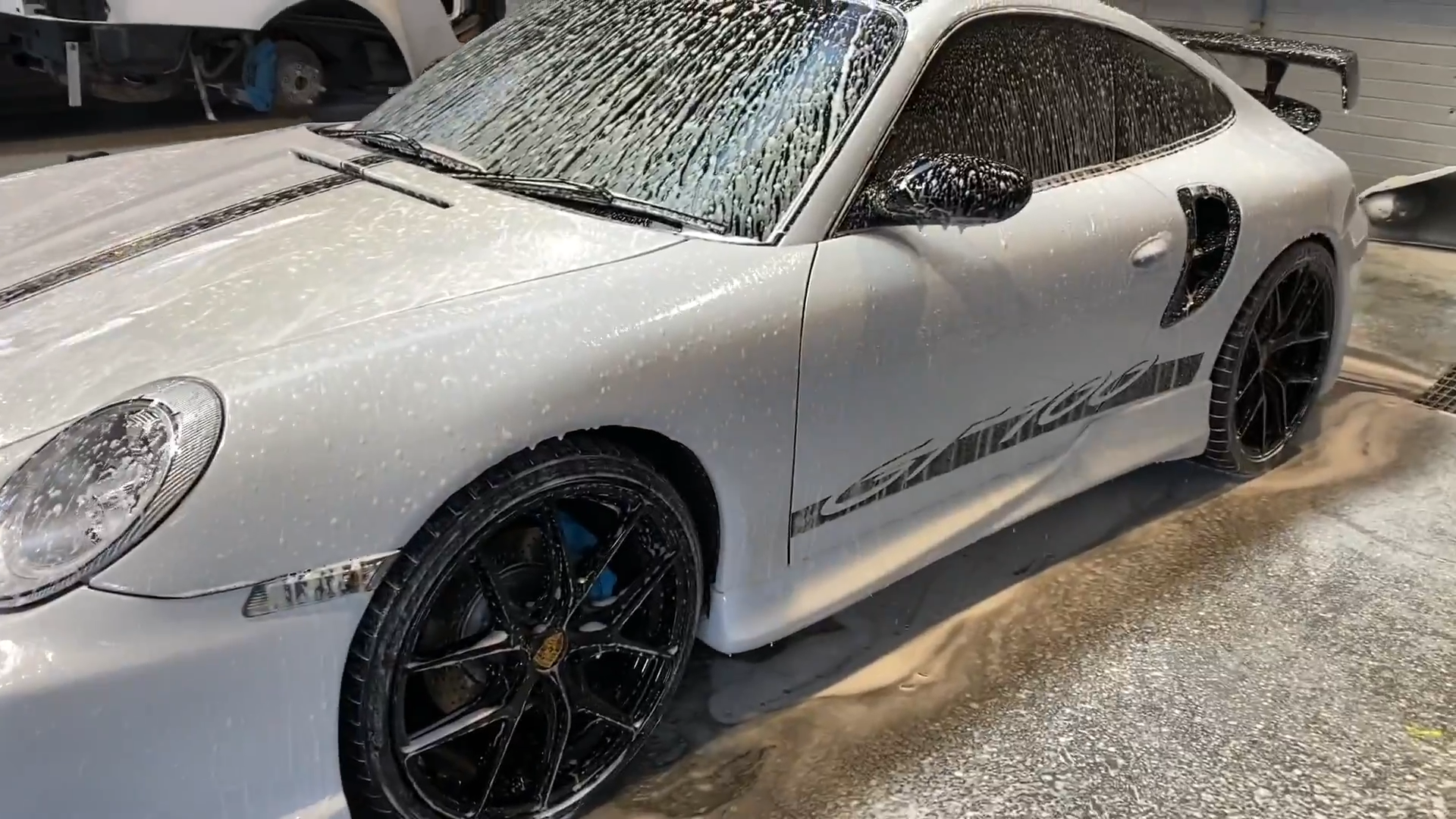 A white luxury sports car with black wheels, covered in soapy foam, inside a garage during a car wash.