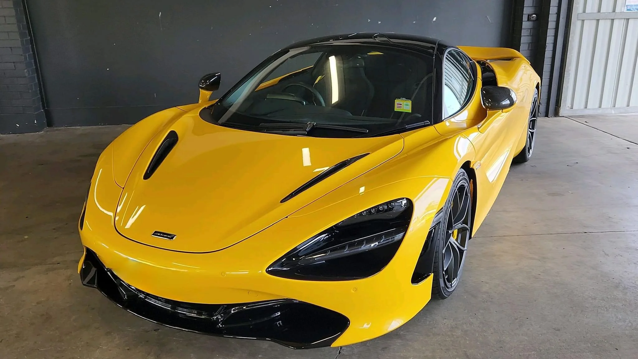 A yellow sports car with black accents parked indoors against a dark wall and partially open white gate.