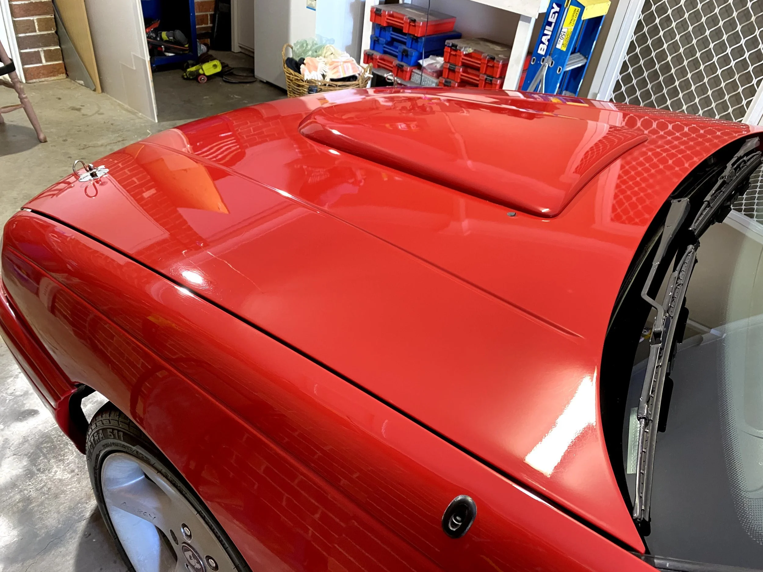A red sports car with its roof partially removed, parked indoors in a garage.