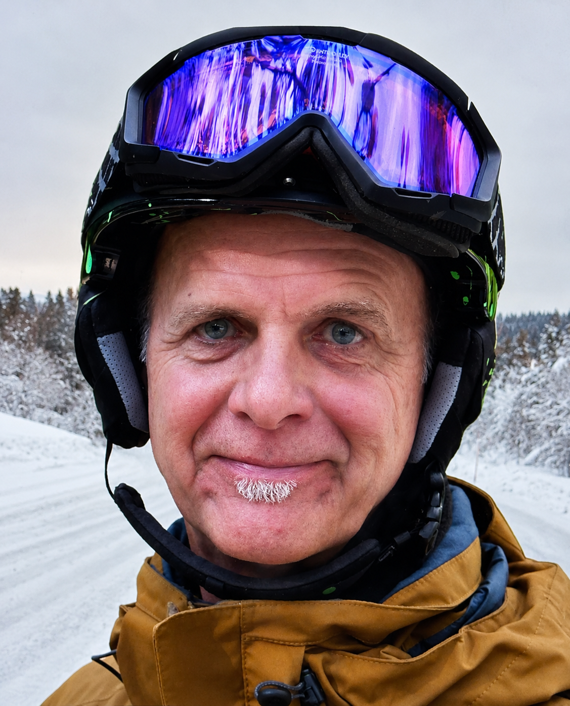 Nahaufnahme eines Mannes mit Skibrille und Winterjacke in verschneiter Landschaft.