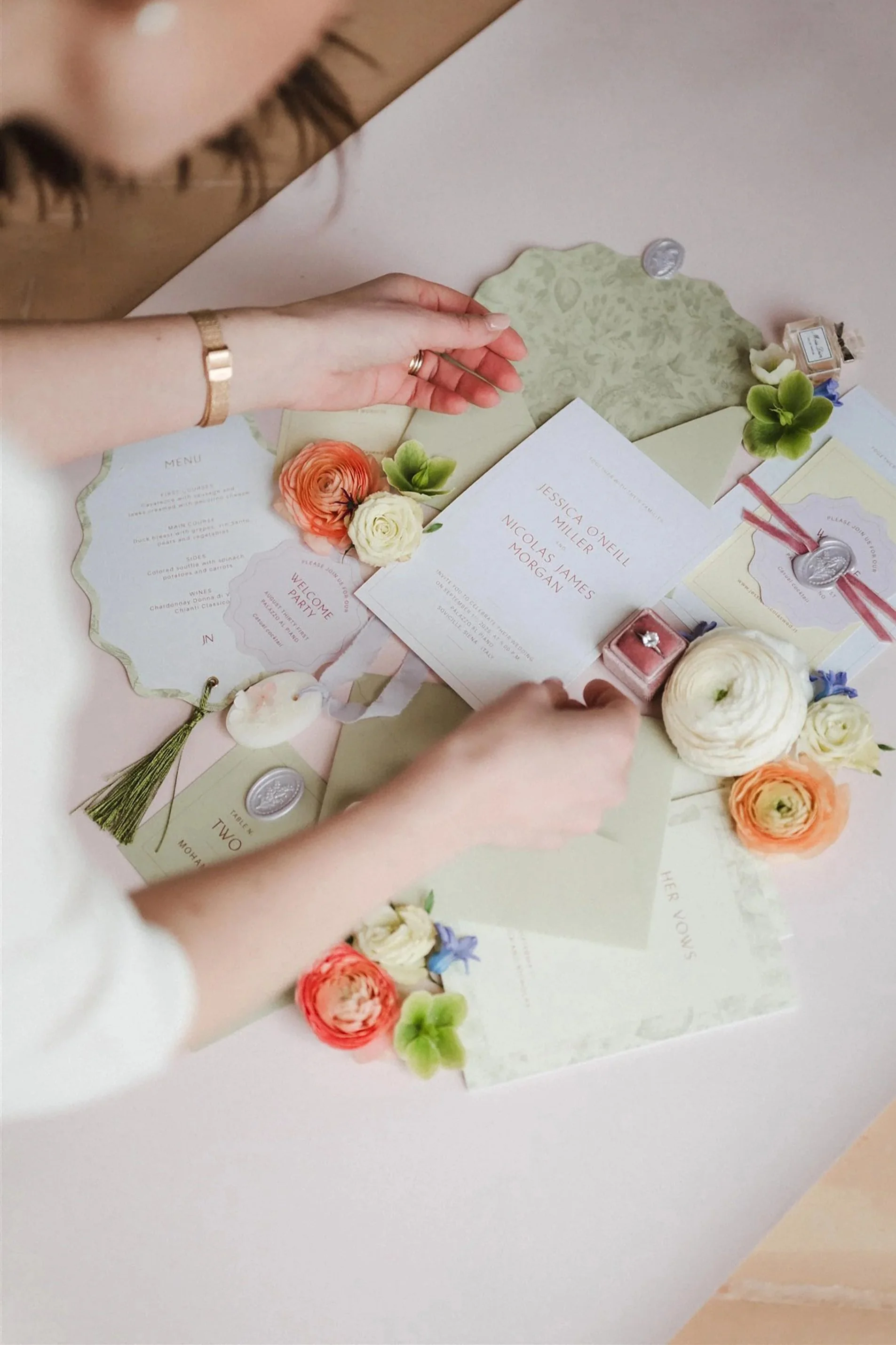 Una persona sta sistemando dettagli di un invito di nozze sulla tavola, decorato con fiori colorati, menu e dettagli in ceralacca.