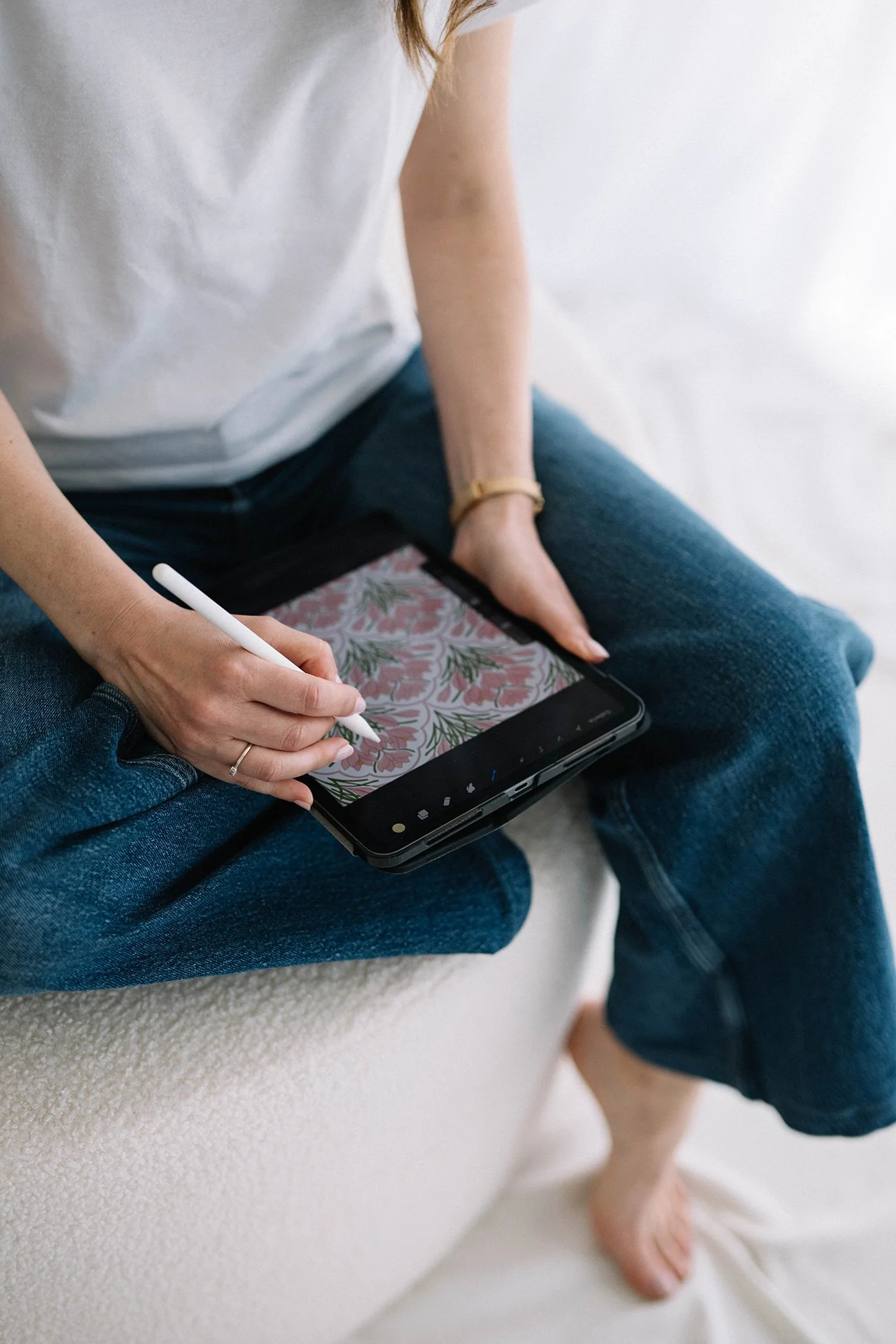 Persona seduta su una sedia con jeans e maglietta bianca, che utilizza la tavoletta grafica per realizzare un pattern floreale.